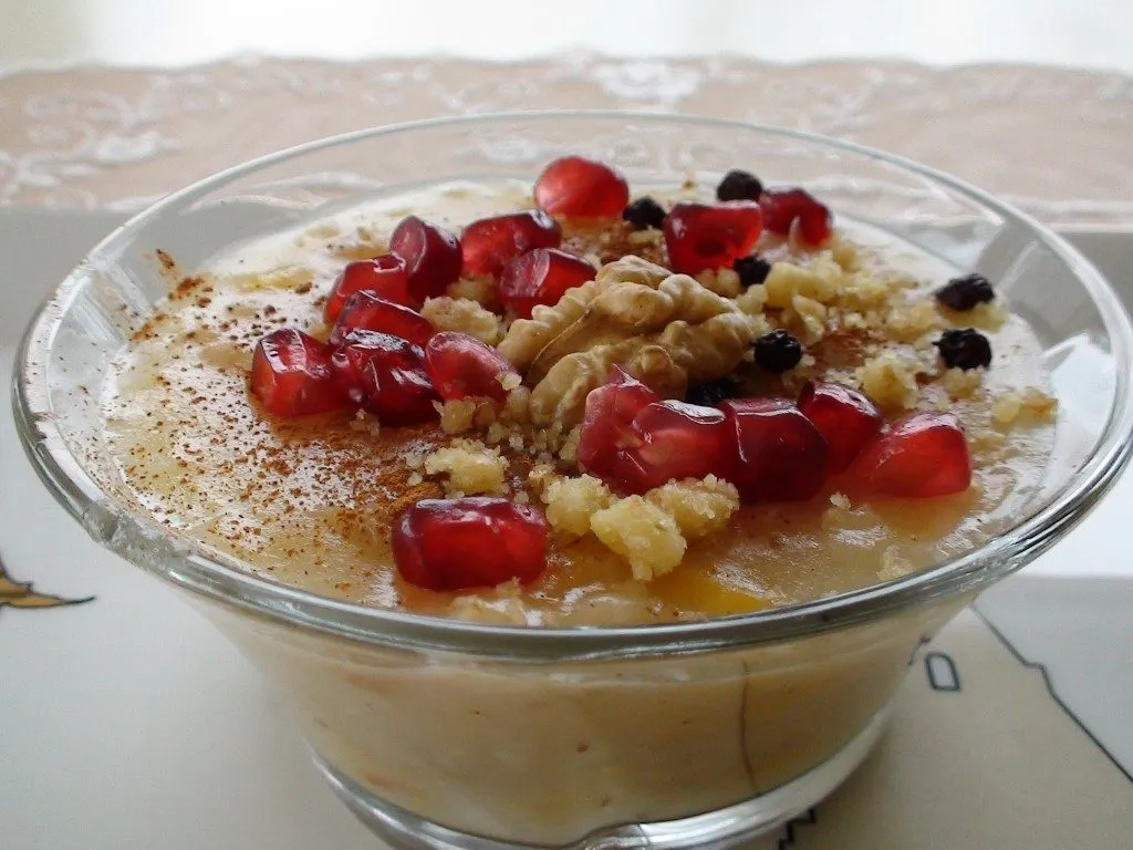 Glass bowl of aşure, noah’s pudding topped with cinnamon, walnuts, currants and pomegranate