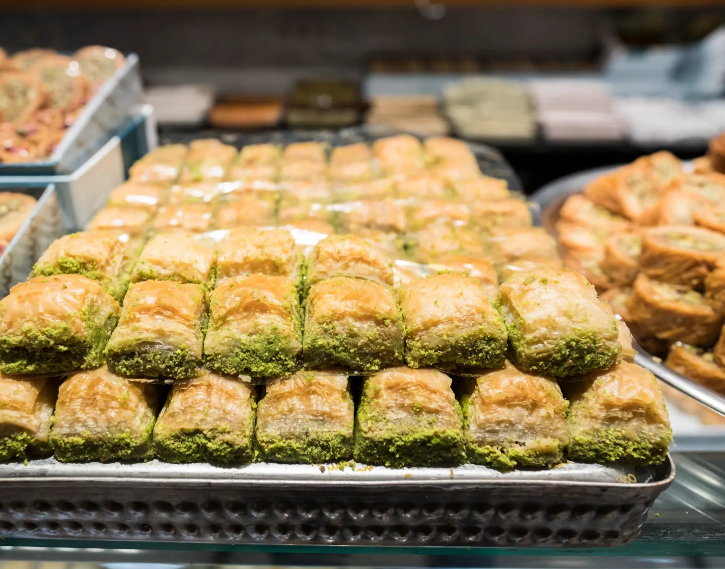 stacked trays of pistachio baklava behind the glass of a sweets-house display case