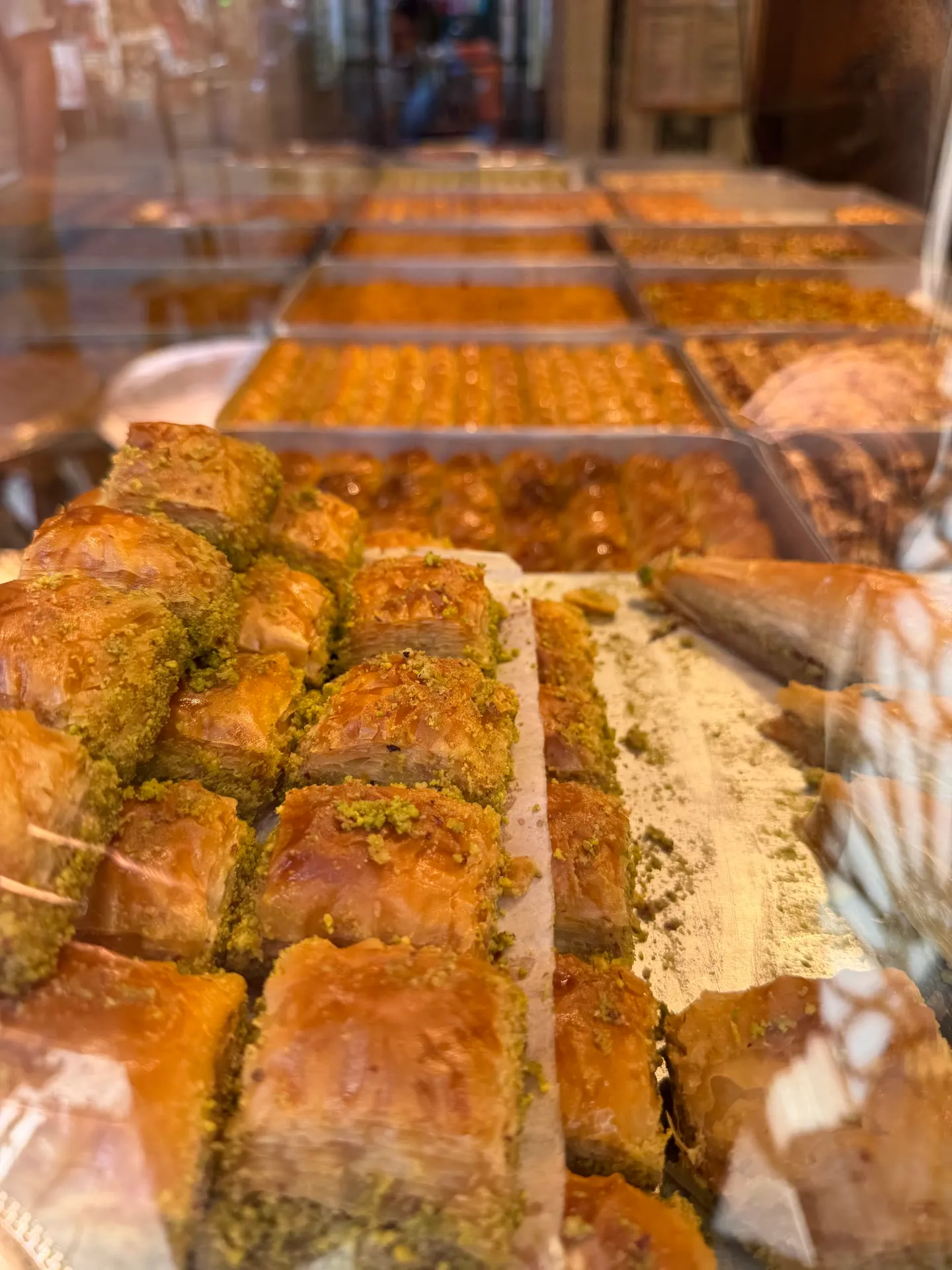 rows of pistachio-topped baklava stacked behind a lit shop window