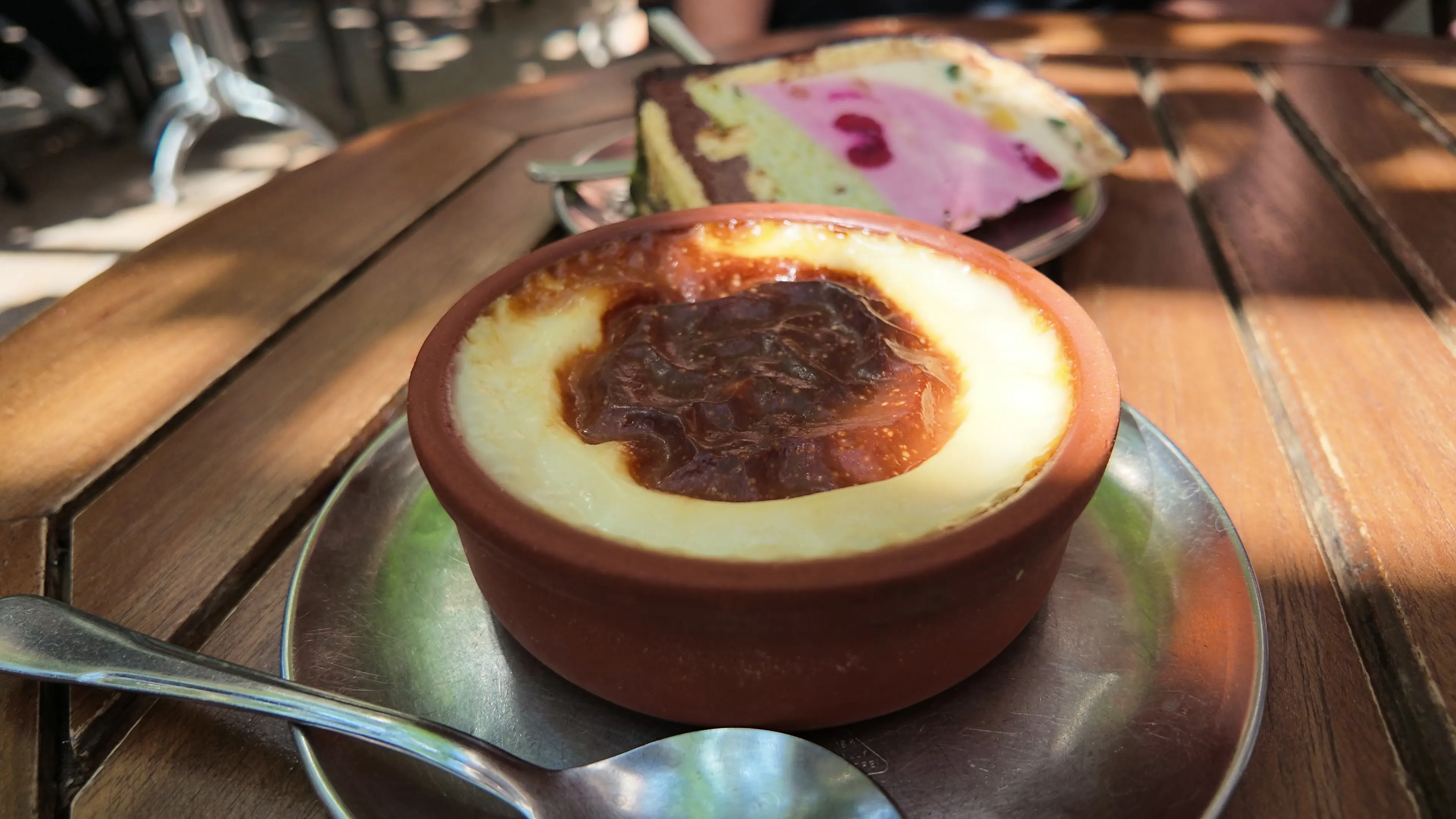 Fırın sütlaç in a clay bowl beside a colorful slice of Adisababa parfait in Baylan's garden