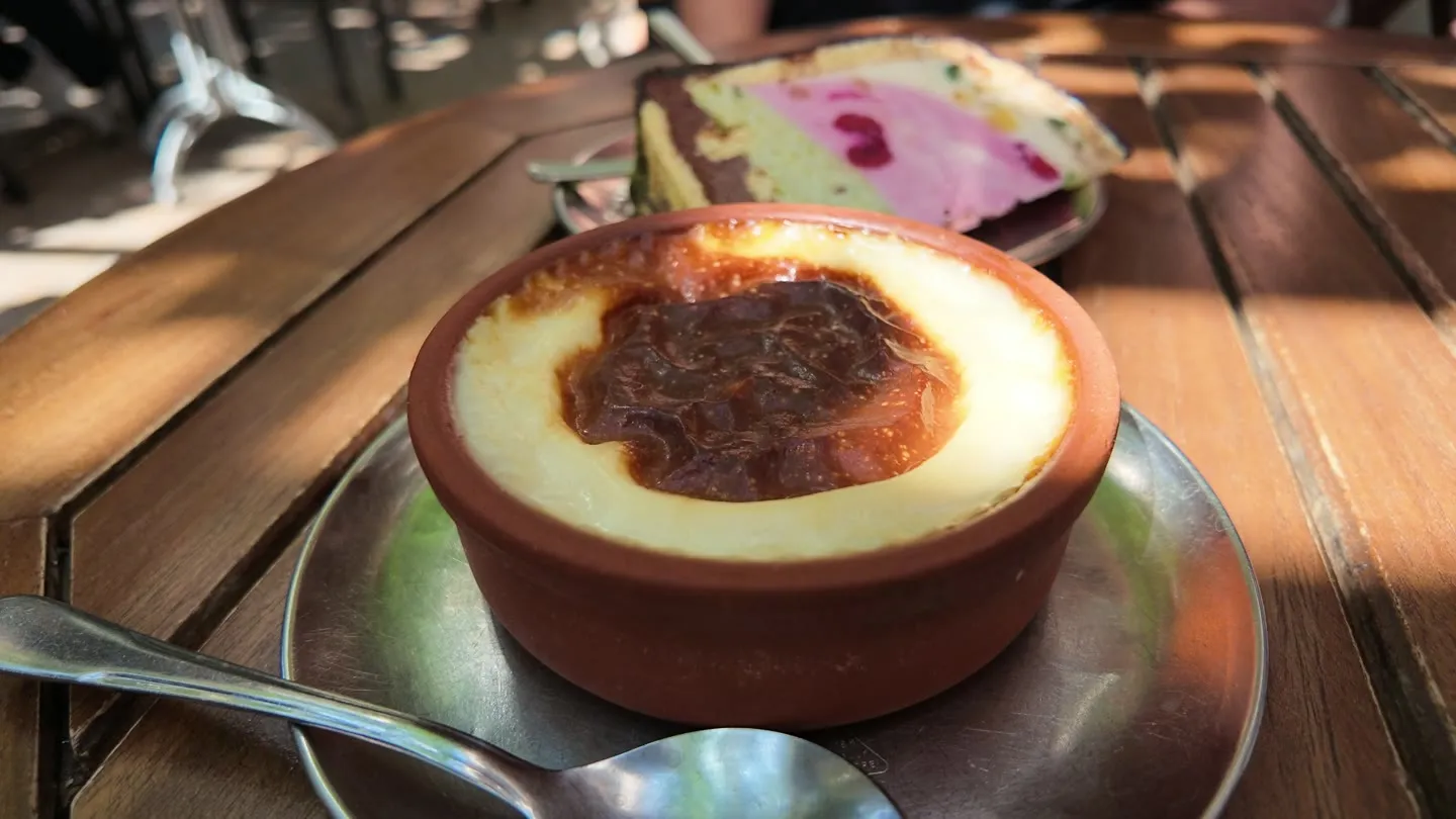firin sutlac in a clay bowl beside a colorful layered slice of Baylan parfait on a wooden table