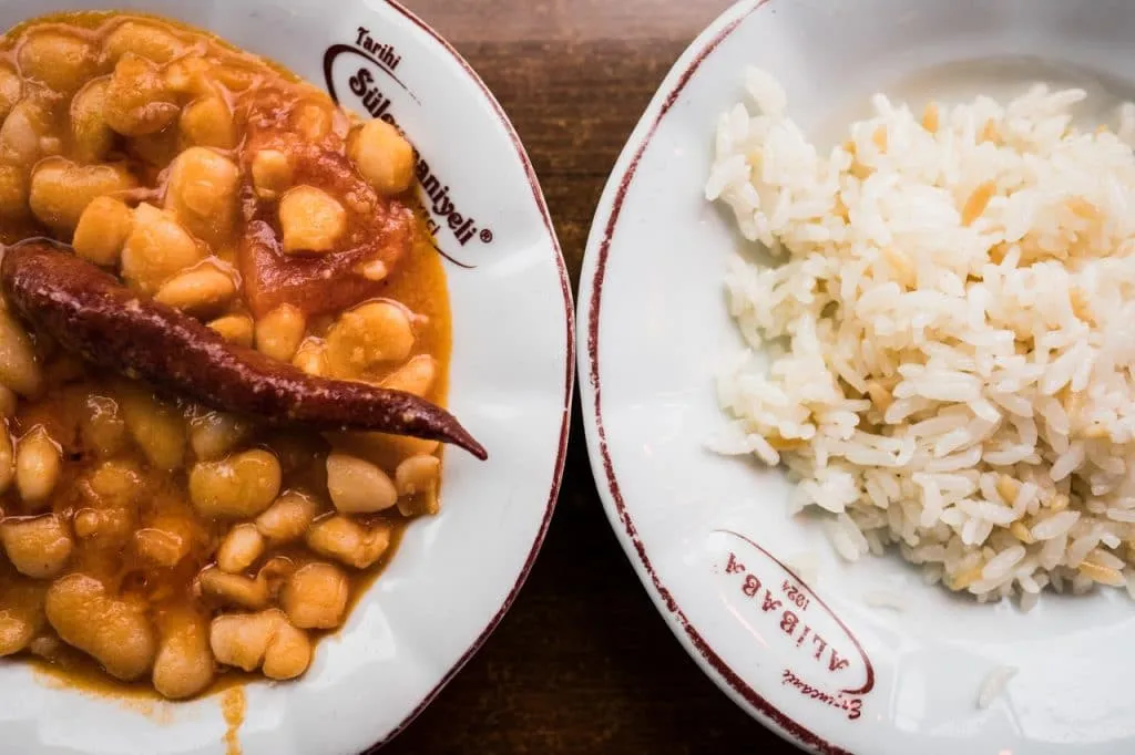 Bowl of Turkish cooked beans with red chilli on top next to bowl of rice pilav