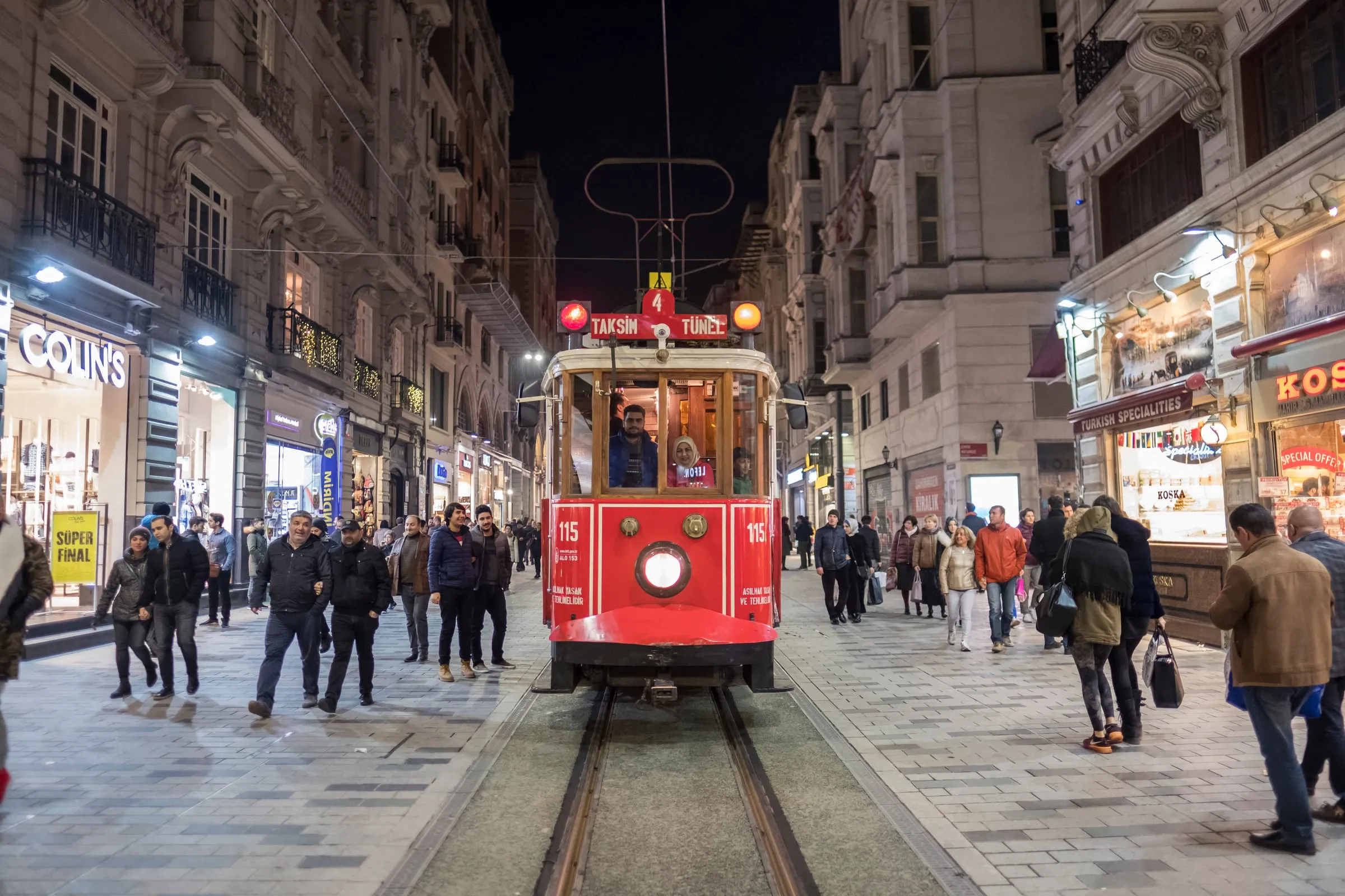 Red nostalgic tram traveling through crowded İstiklal Avenue at night