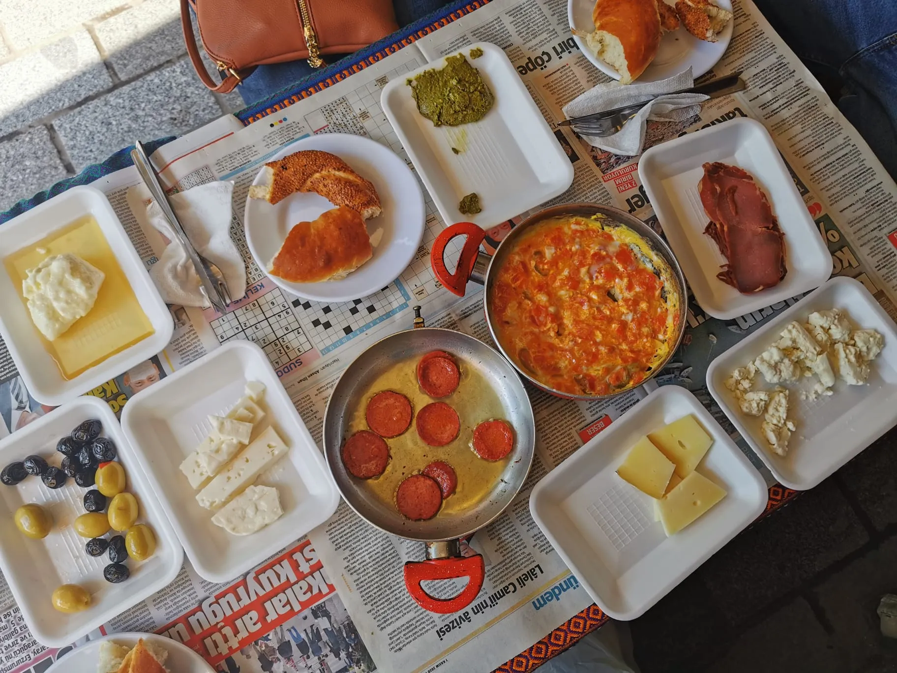 Small plates of cheese, olives, sweet spreads, and vegetables around hot breakfast pans