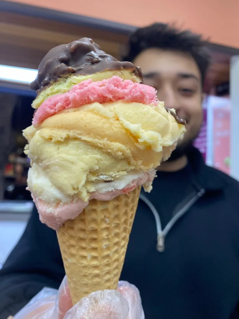 A tall multi-scoop cone of Bu & Bu Dondurma, chocolate-dipped on top with strawberry and cream scoops on a waffle cone