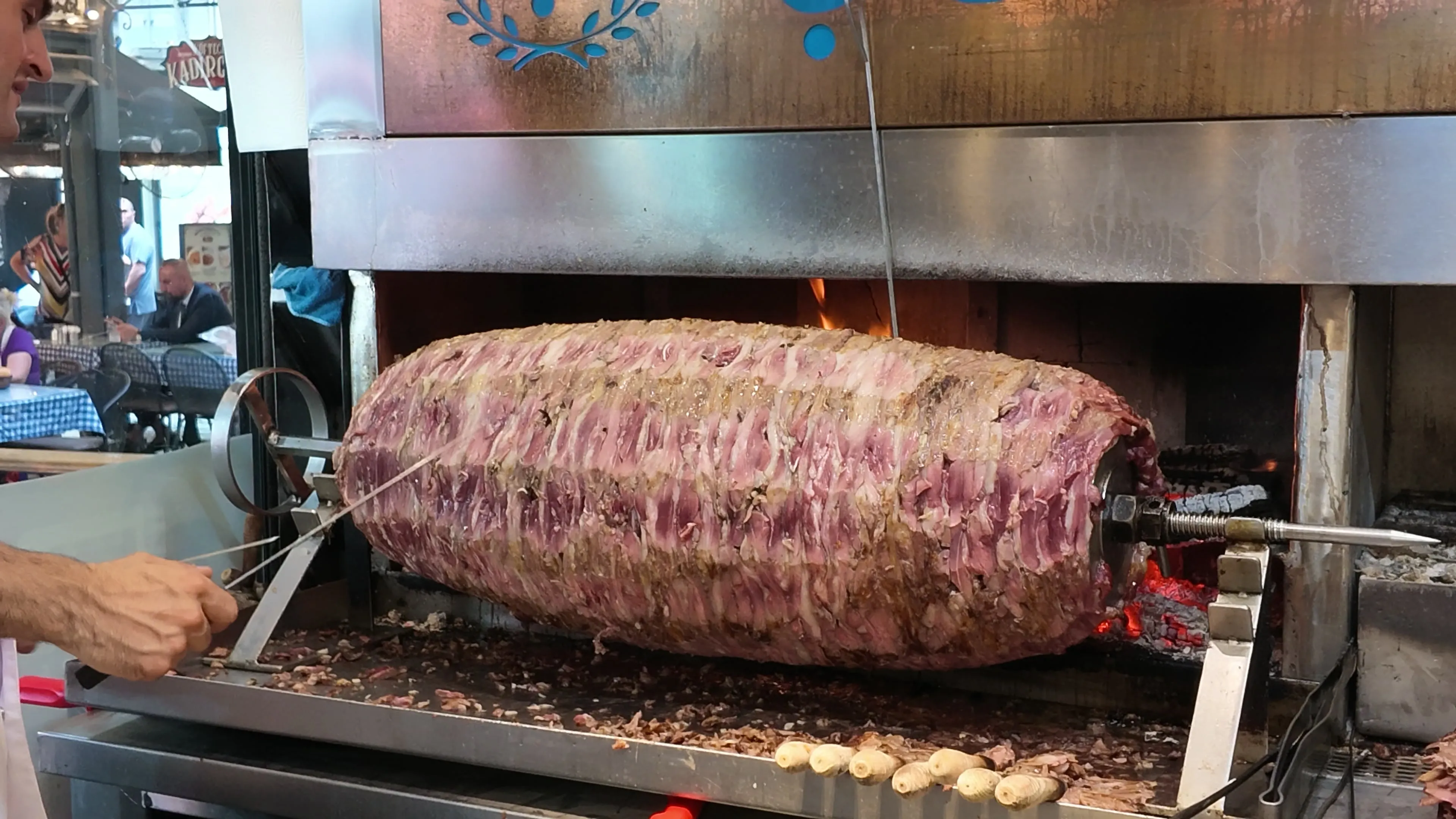A large cağ kebabı roasting on a horizontal spit in front of an open hearth