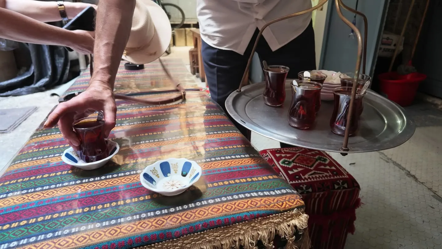 A server's hanging tray delivers tulip glasses of tea to a bench at a courtyard çay ocağı