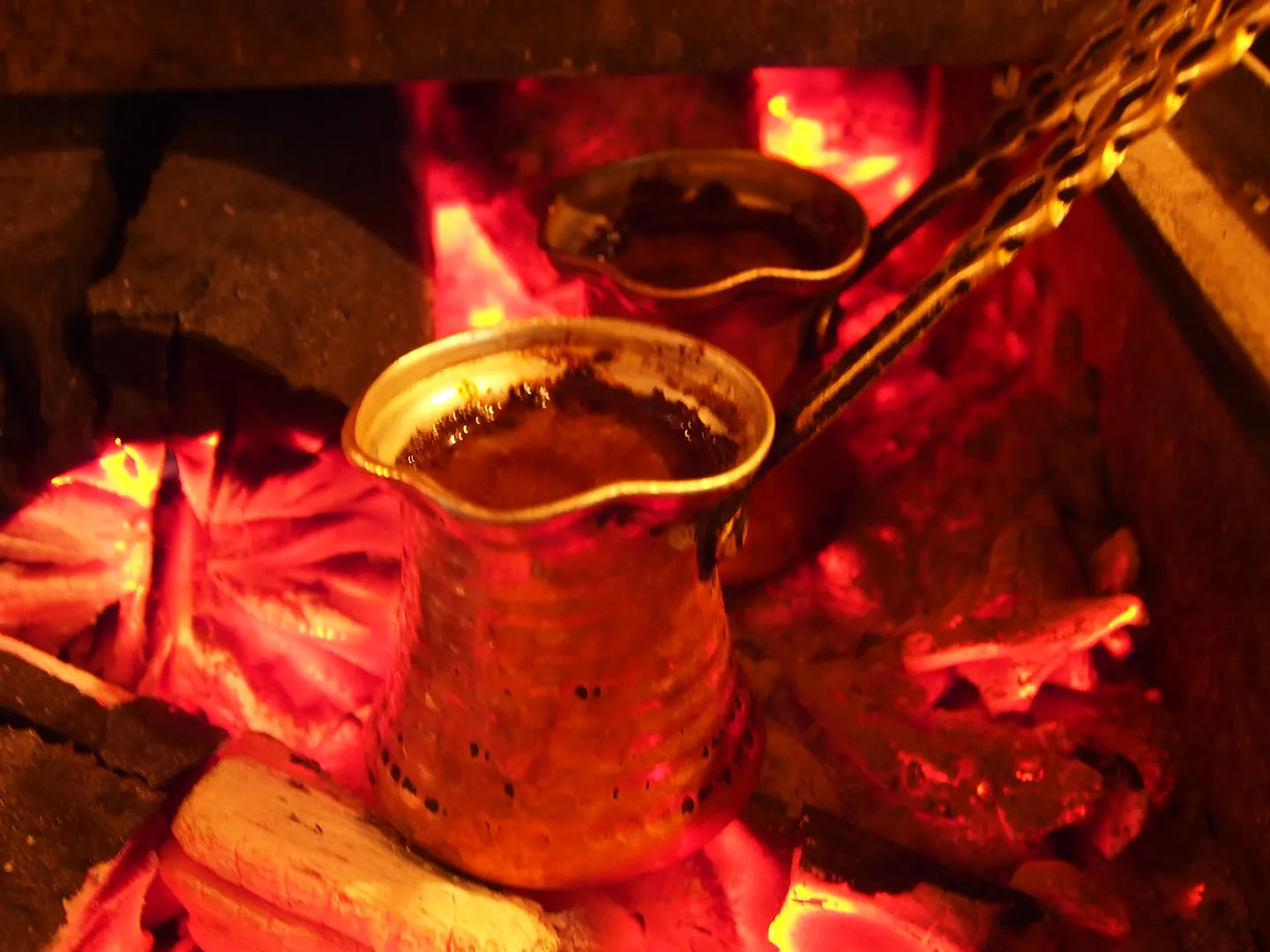 copper cezve of Turkish coffee foaming over glowing charcoal