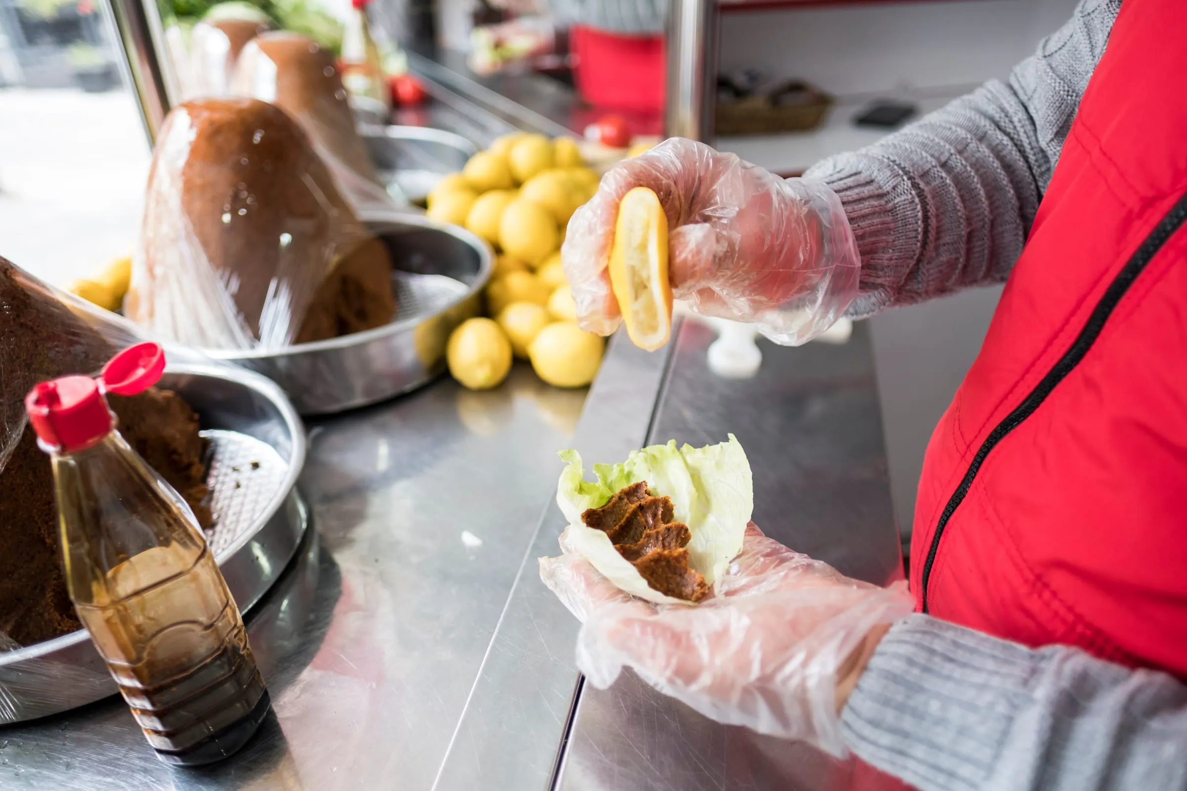Vendor squeezing lemon over a çiğ köfte lettuce wrap at an Istanbul counter, with cones of çiğ köfte behind