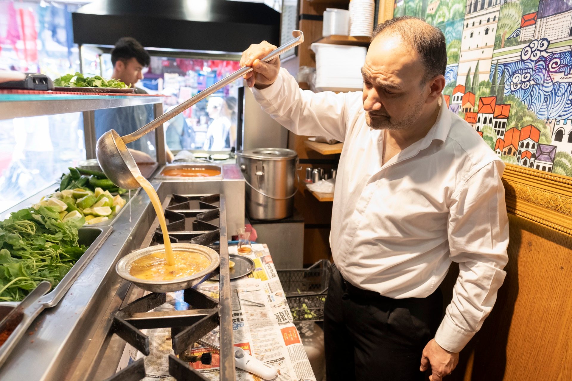 Cook ladling hot beyran broth from a large pot in an Istanbul kitchen
