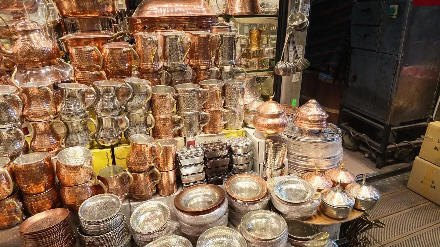 a copper workshop storefront stacked with hammered pots, jugs, lidded bowls and trays