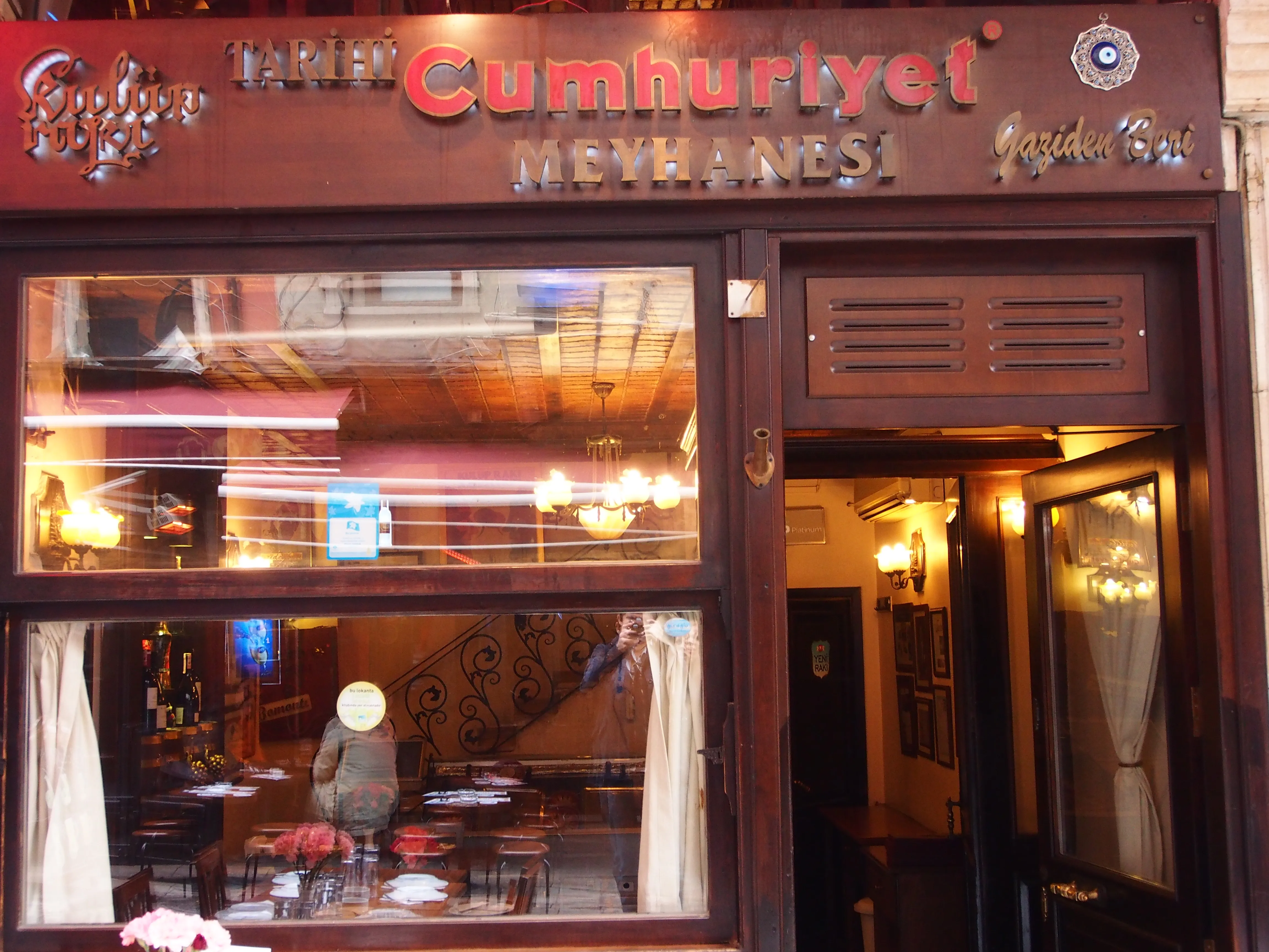 The red Cumhuriyet Meyhanesi sign hangs above an illuminated restaurant entrance