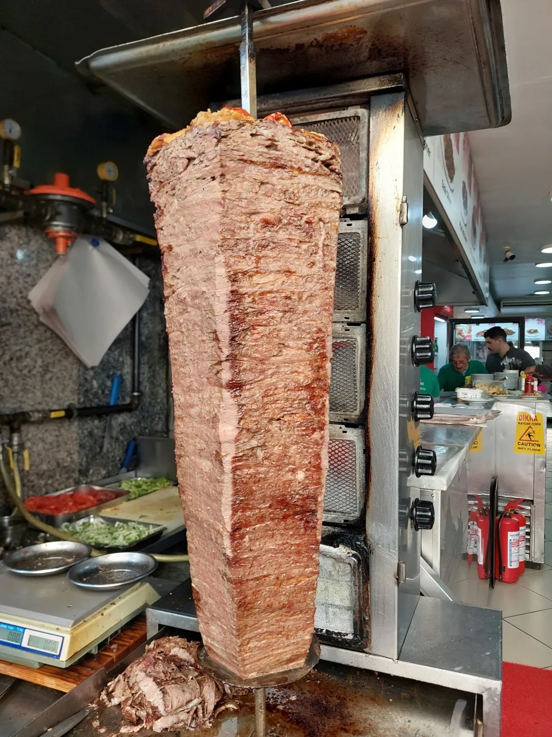 tall doner cone with browned edges turning on a vertical spit, carved pieces at its base