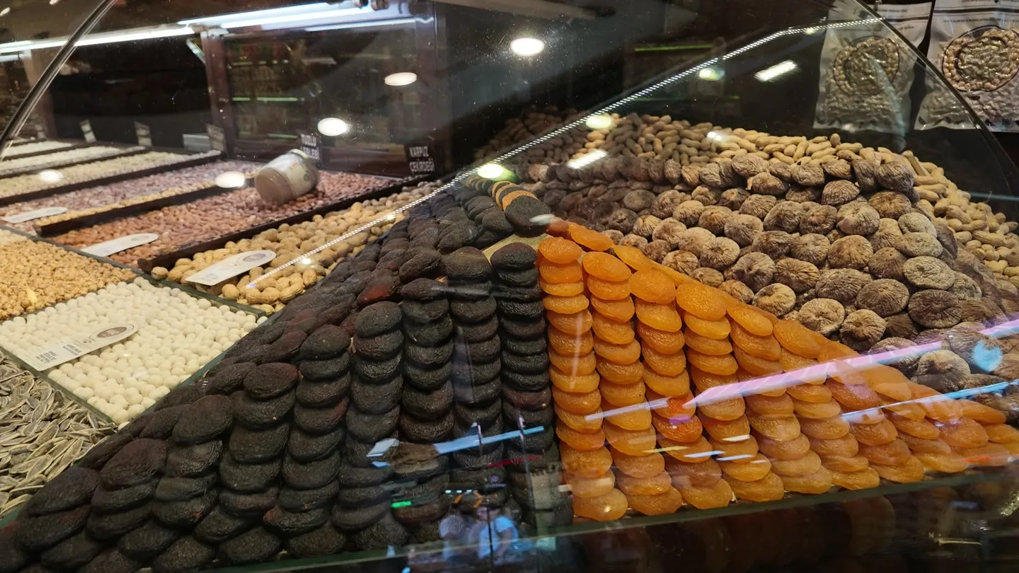 stacked rows of black and orange dried apricots, figs and nuts arranged behind a glass counter