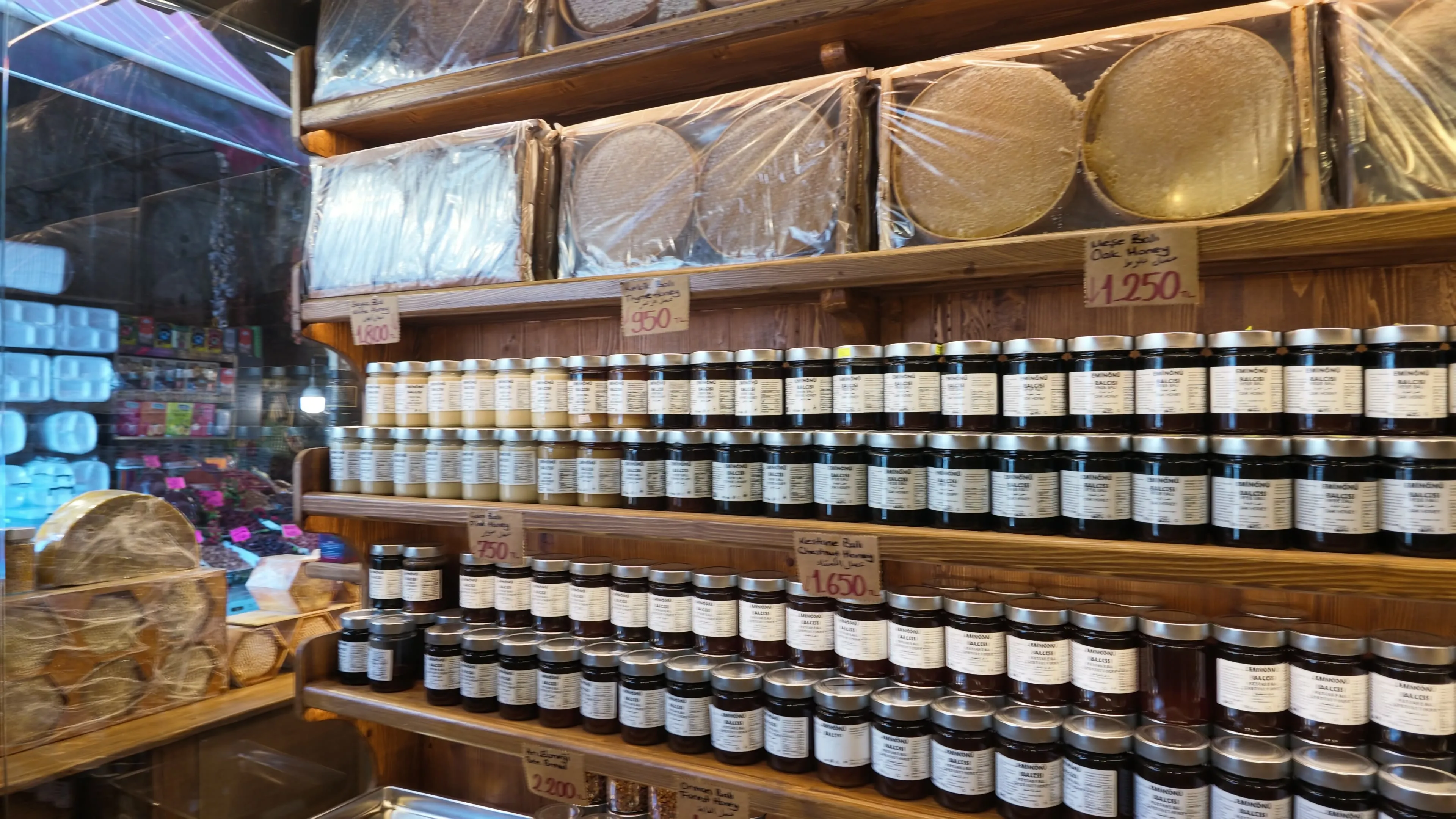 Rows of honey jars and large wrapped honeycombs line wooden shelves