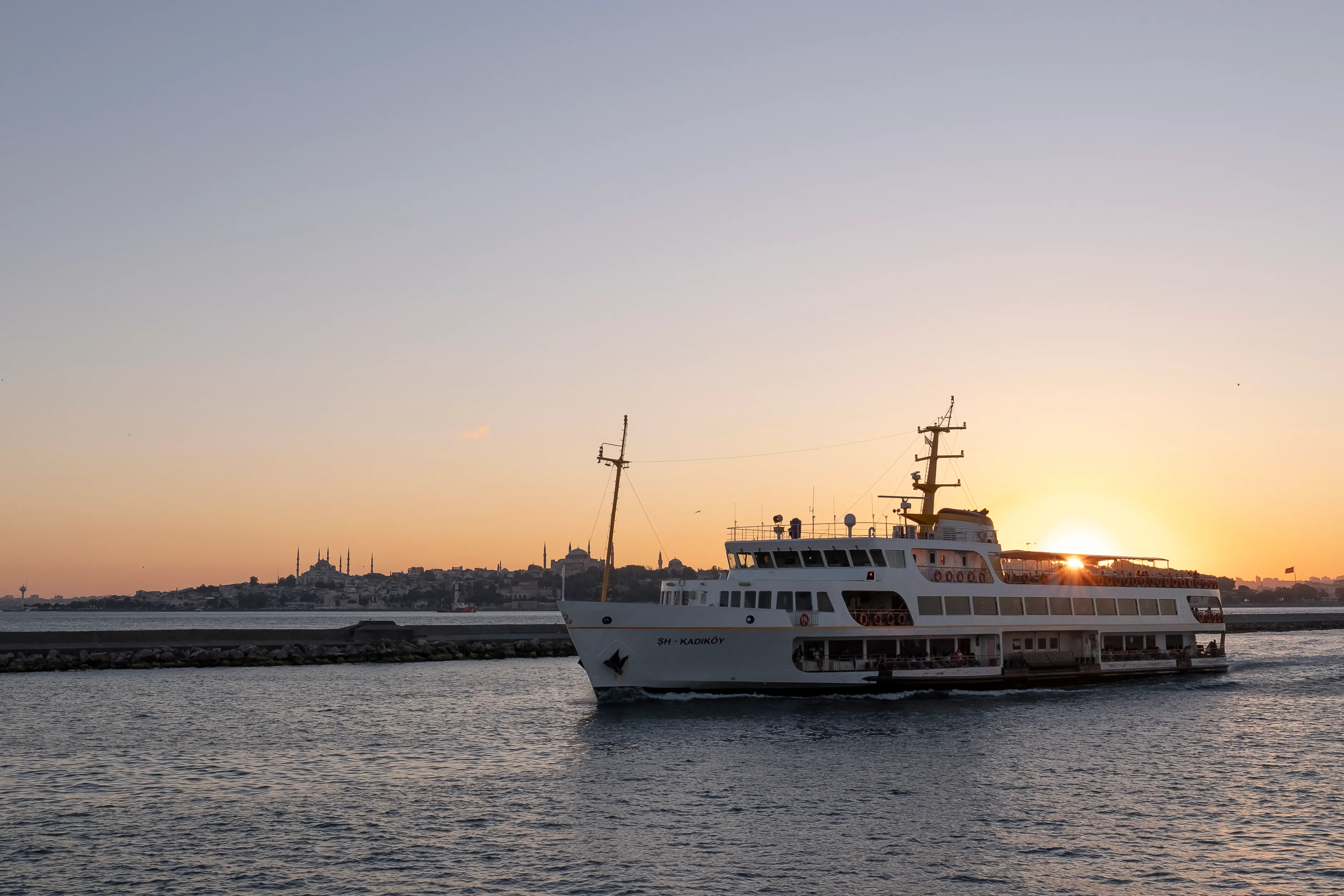 A white passenger ferry passes Istanbul's old-city skyline as the sun sets