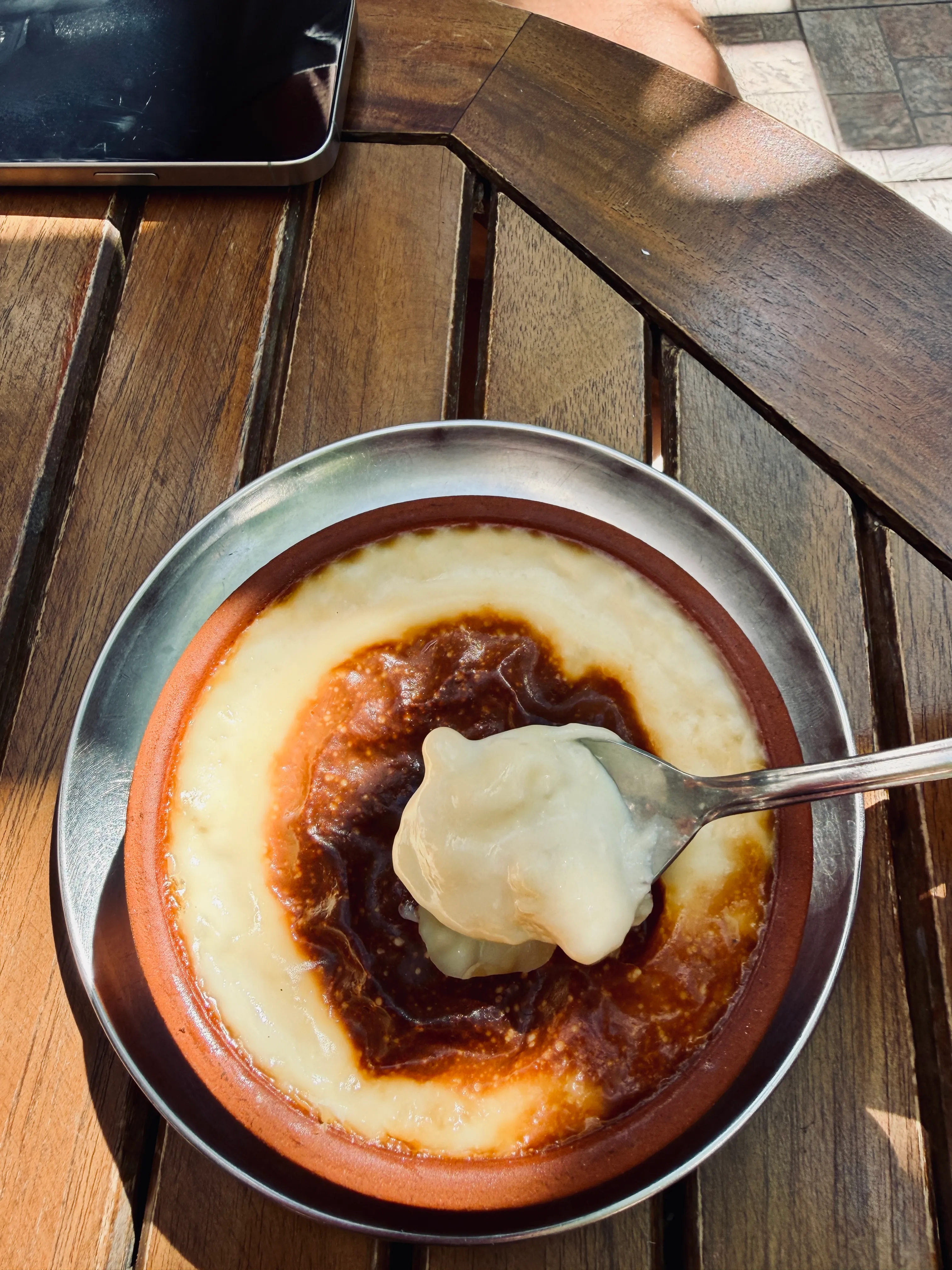 Oven-finished rice pudding in a clay bowl, with a spoonful lifted above it