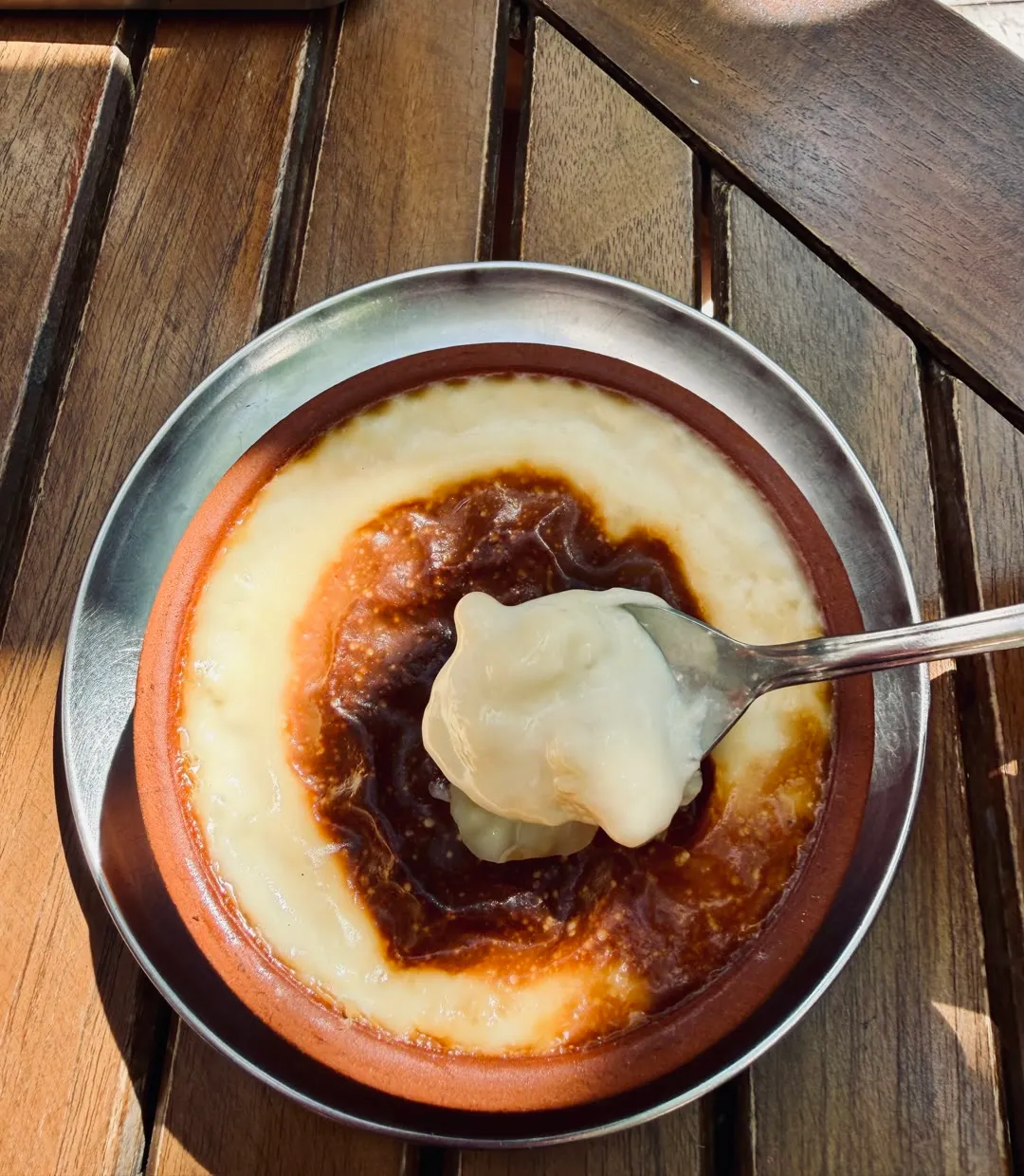 firin sutlac in a clay bowl with a caramelized top, a spoonful lifted out