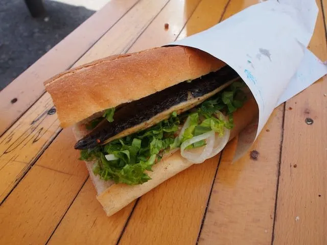 Bread roll fish sandwich filled with fish, lettuce, onion wrapped in paper on wooden table