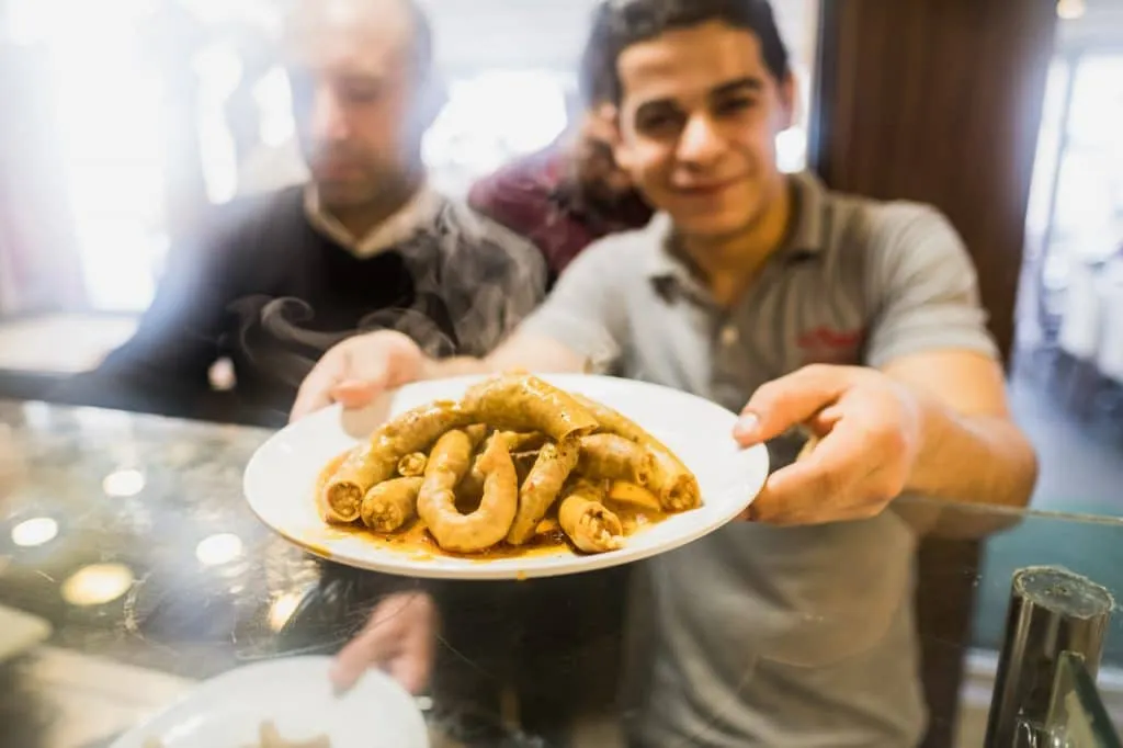 Smiling waiter offering us a plate of mumbar (stuffed intestines) during flavors of old city tour