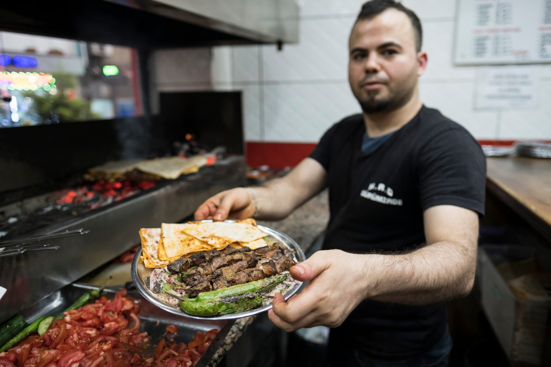 Cook holding a plate of grilled kebab on lavash with a grilled green pepper in Istanbul