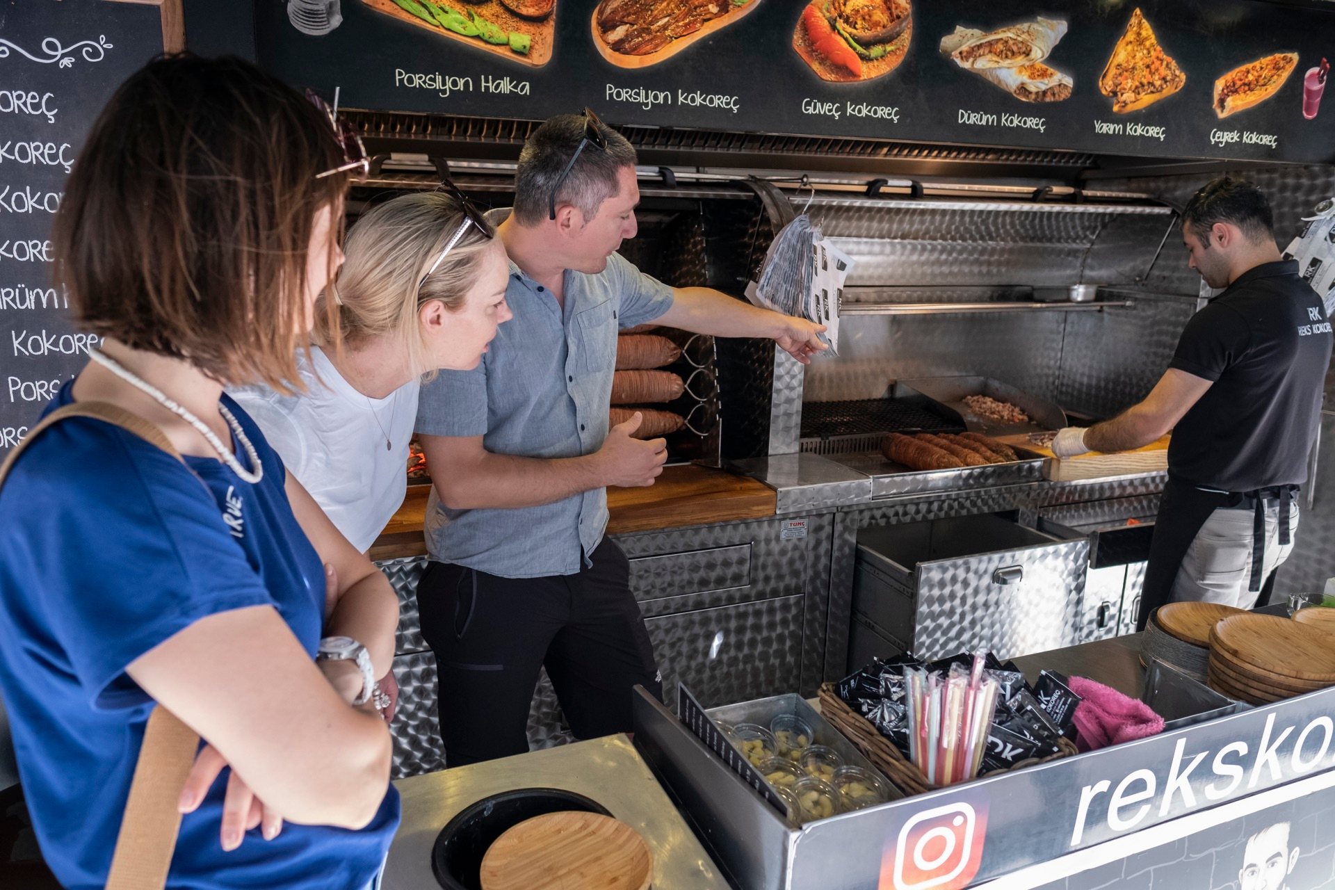 Tour guests watching a vendor grill kokoreç at a Kadıköy street counter in Istanbul
