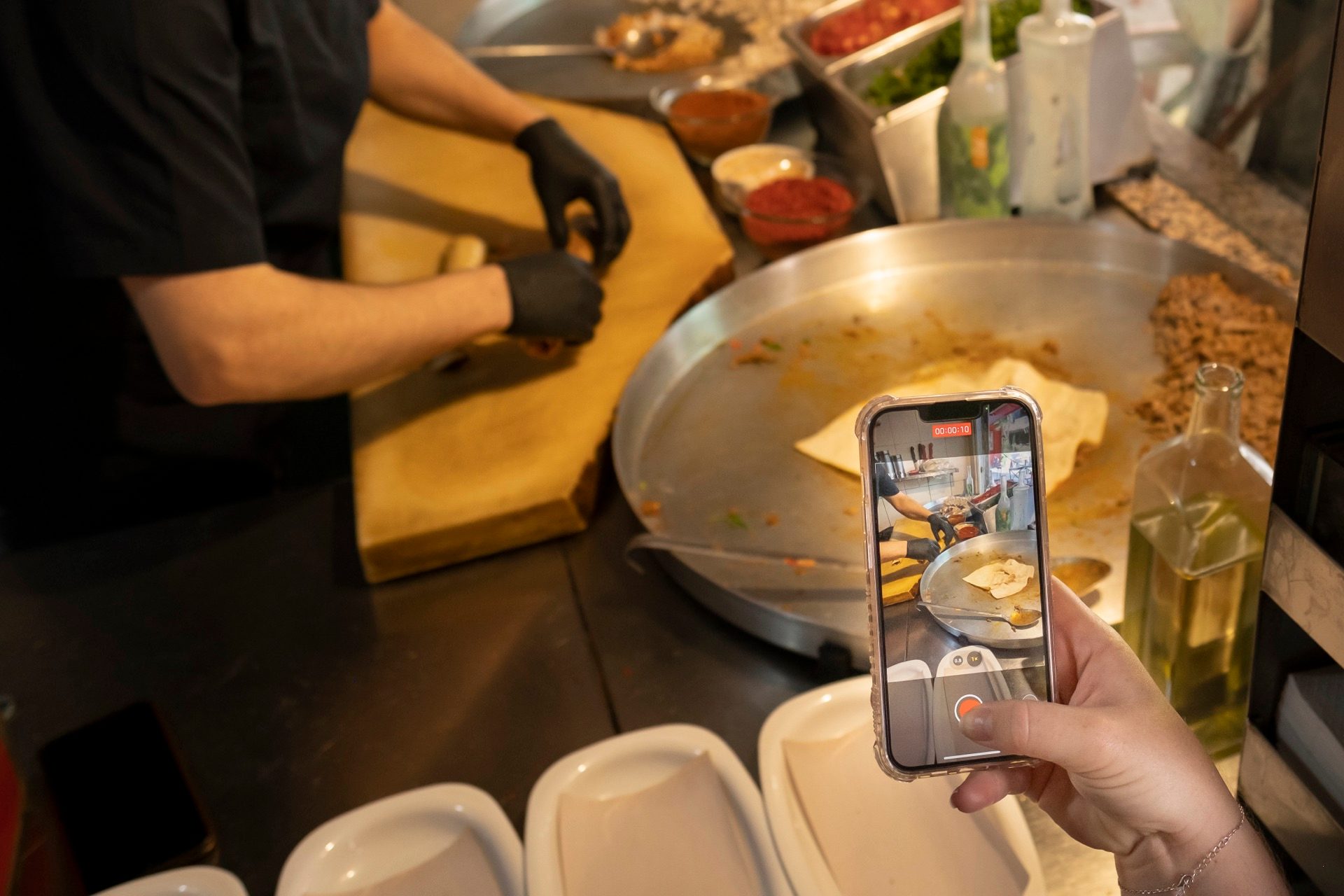 Guest filming a Kadıköy street-food vendor cooking at a wide griddle in Istanbul