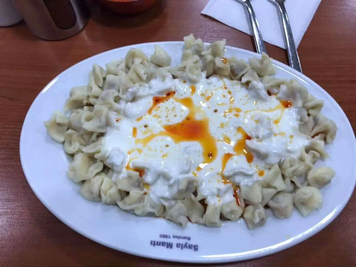 Plate of Turkish manti dumplings topped with yogurt and red pepper sauce on a table