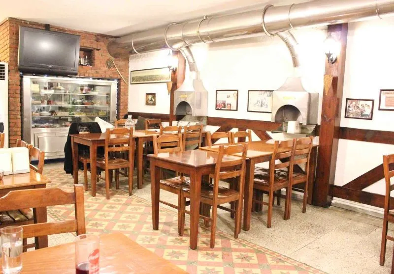 Empty restaurant with wooden tables, patterned tile floor, and charcoal grill hoods on the wall