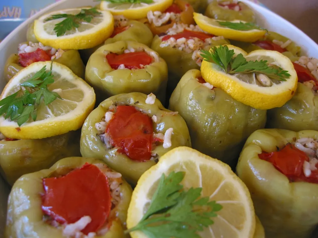 Tray of green peppers stuffed with rice topped with tomatoes and lemons