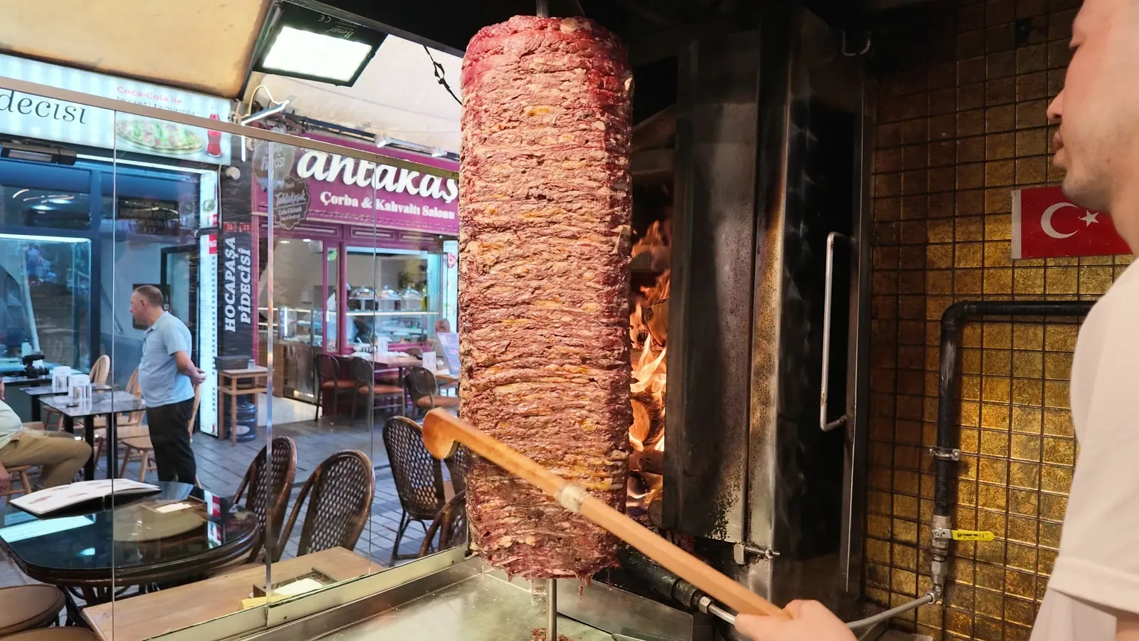 cook beside a wood-fired doner kebab stack turning on its spit at an Istanbul counter