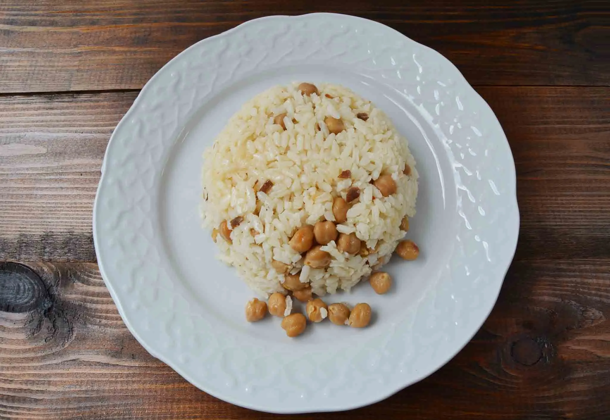 Mound of Turkish rice pilaf with chickpeas on a white plate over a wooden table