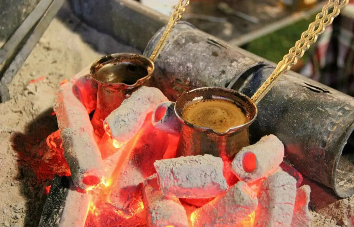 Two brass Turkish coffee posts being roasted traditionally in wood coals