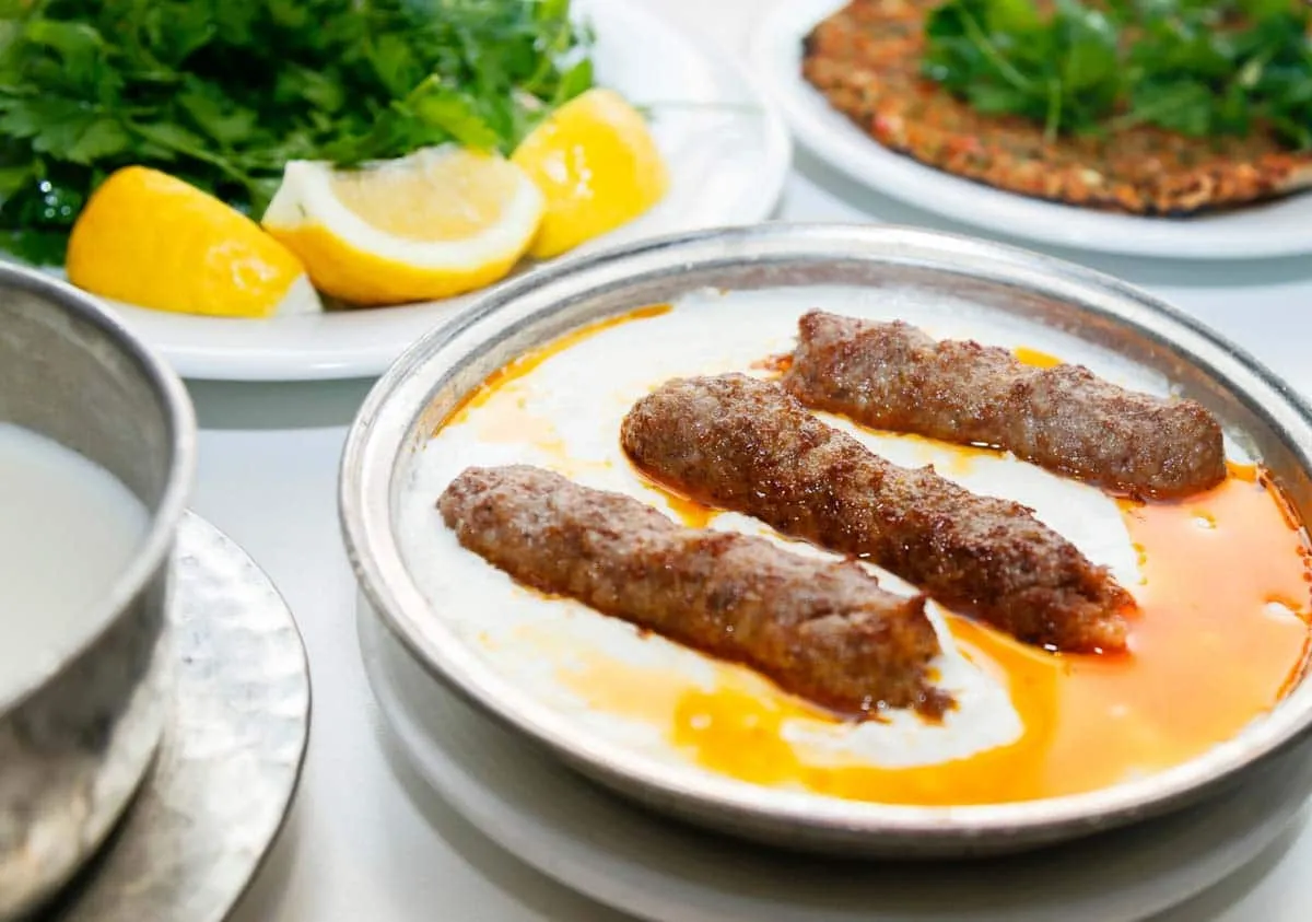 Grilled Adana kebab on a metal plate with parsley, lemon wedges, and lahmacun nearby