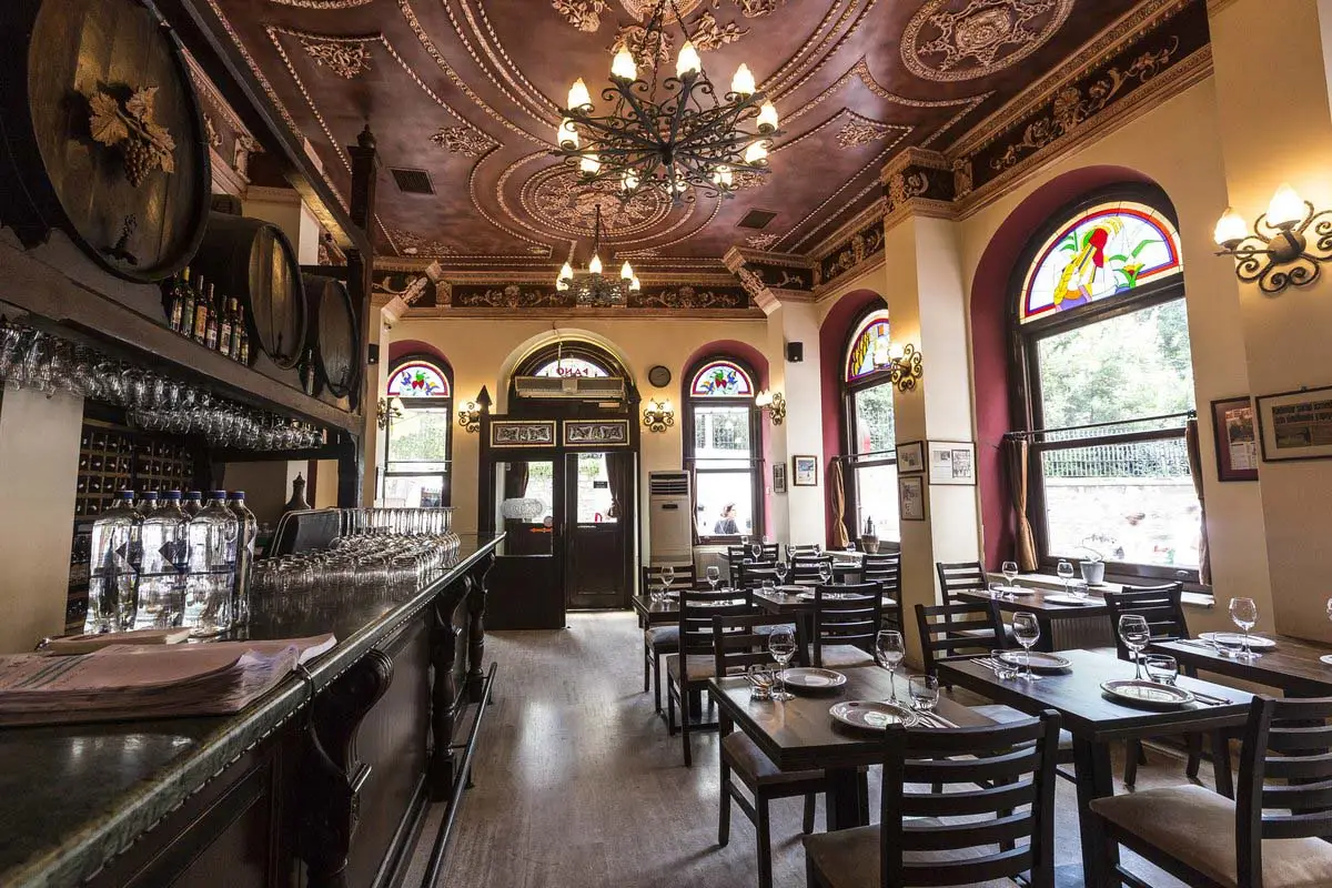 Empty traditional restaurant with a wooden bar, ornate ceiling, chandeliers, and set tables