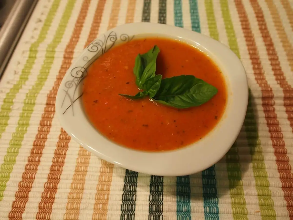 Small bowl of turkish tomato soup topped with fresh basil leaves on striped tablecloth