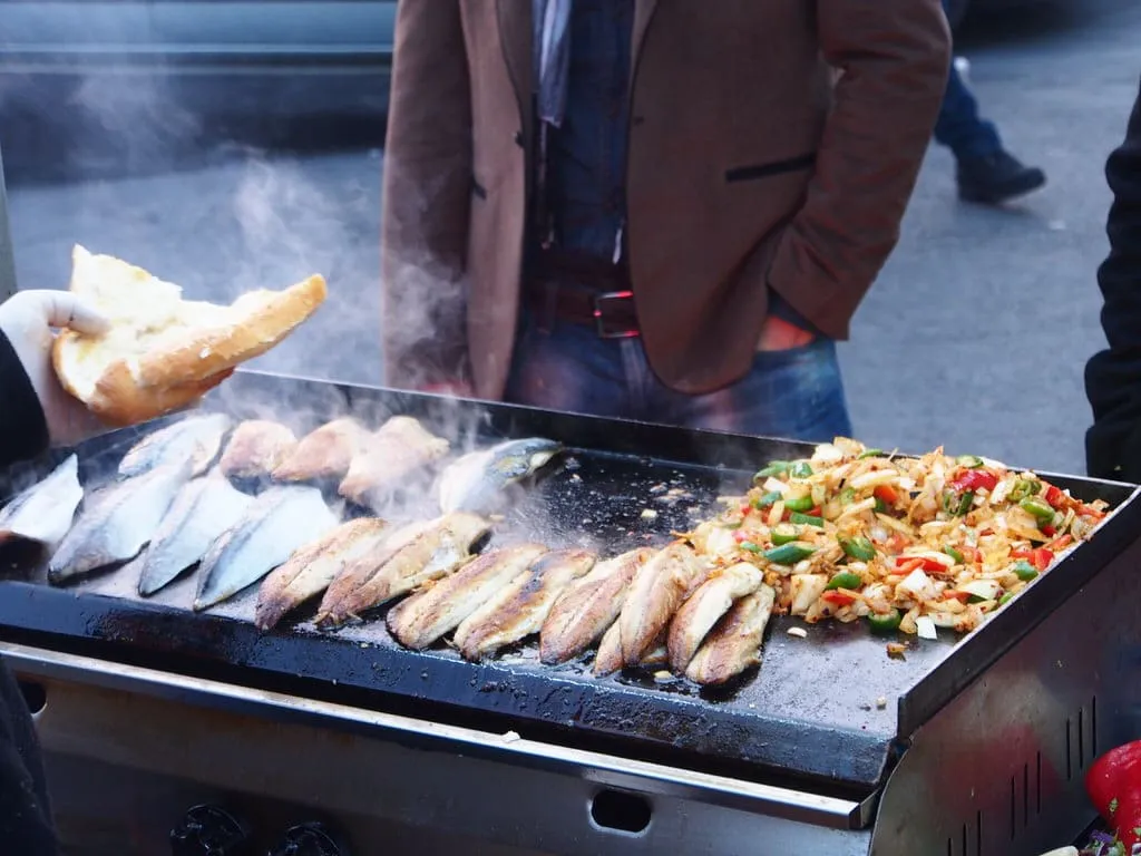 Street vendor barbeque cooking fresh fish with vegetables to fill bread roll for local fish sandwich