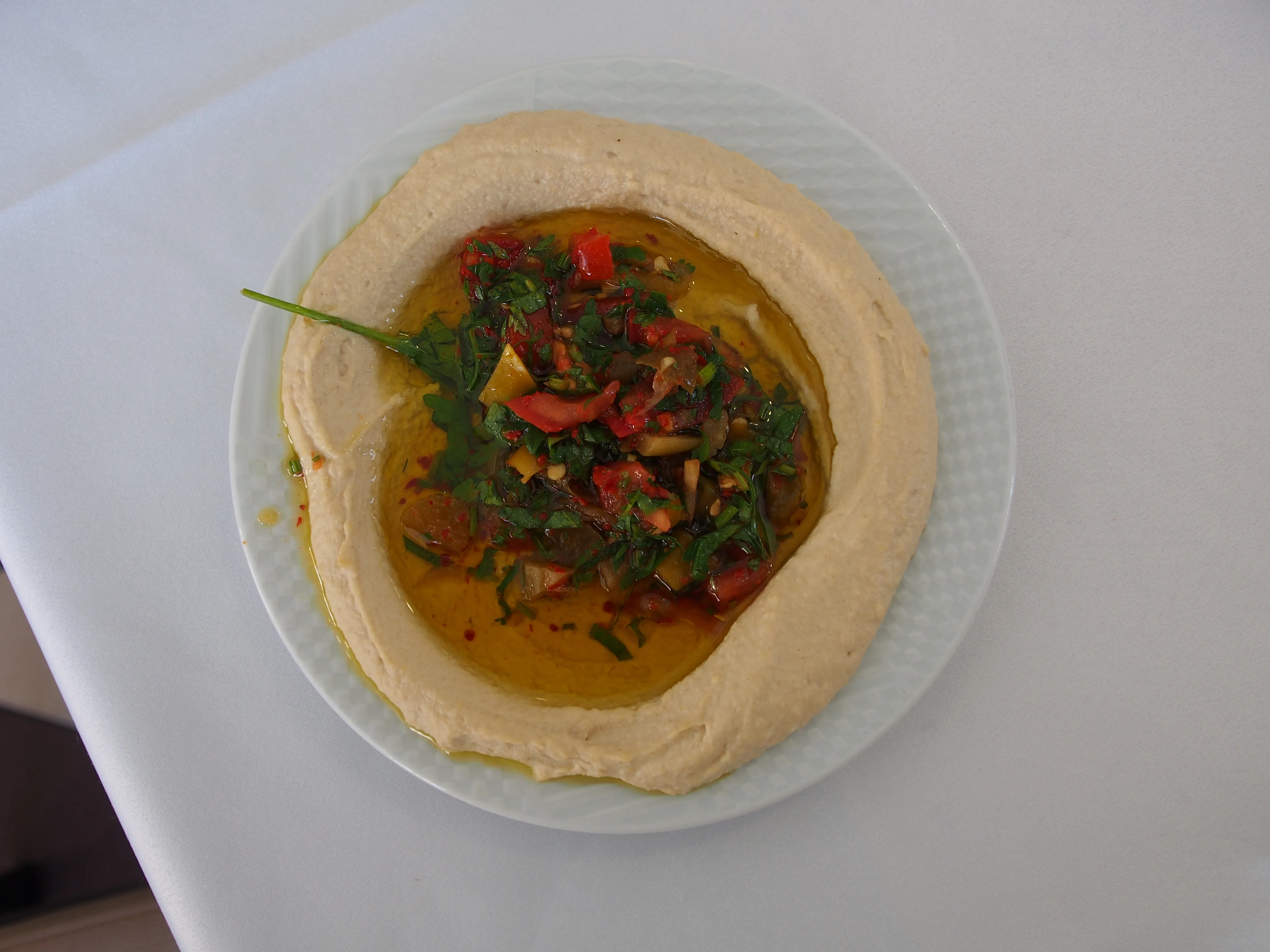 Hummus topped with chopped vegetables, herbs, and oil on a white plate