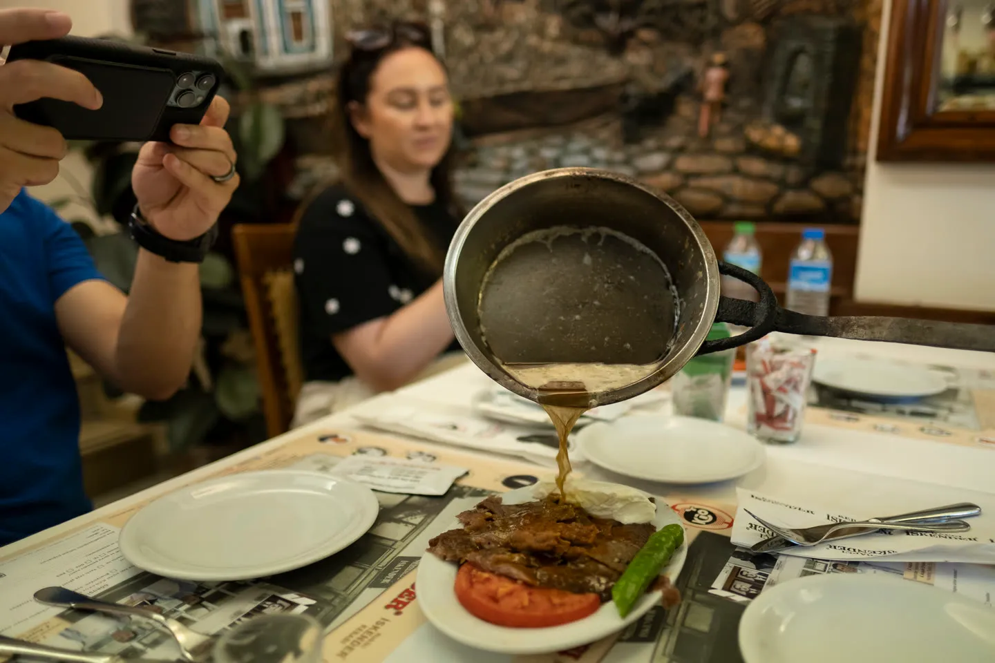 server pours melted butter from a pan over an iskender kebab plate at the table
