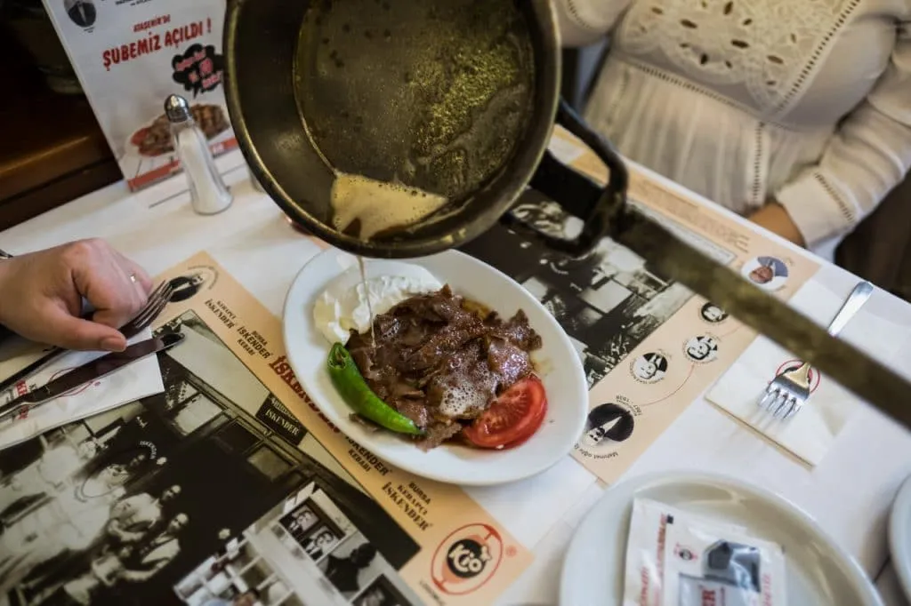 Pouring melted butter from pan over portion of iskender kebab at istanbul restaurant during food tour