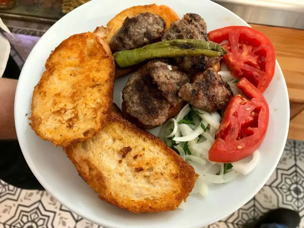 Plate of ıslama köfte at AKO in Kadıköy: grilled meatballs over broth-soaked bread with tomato, onion, and a grilled pepper