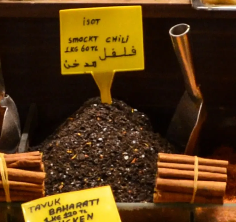 Yellow sign reading isot smoked chili over a pile of nearly black isot pepper flakes
