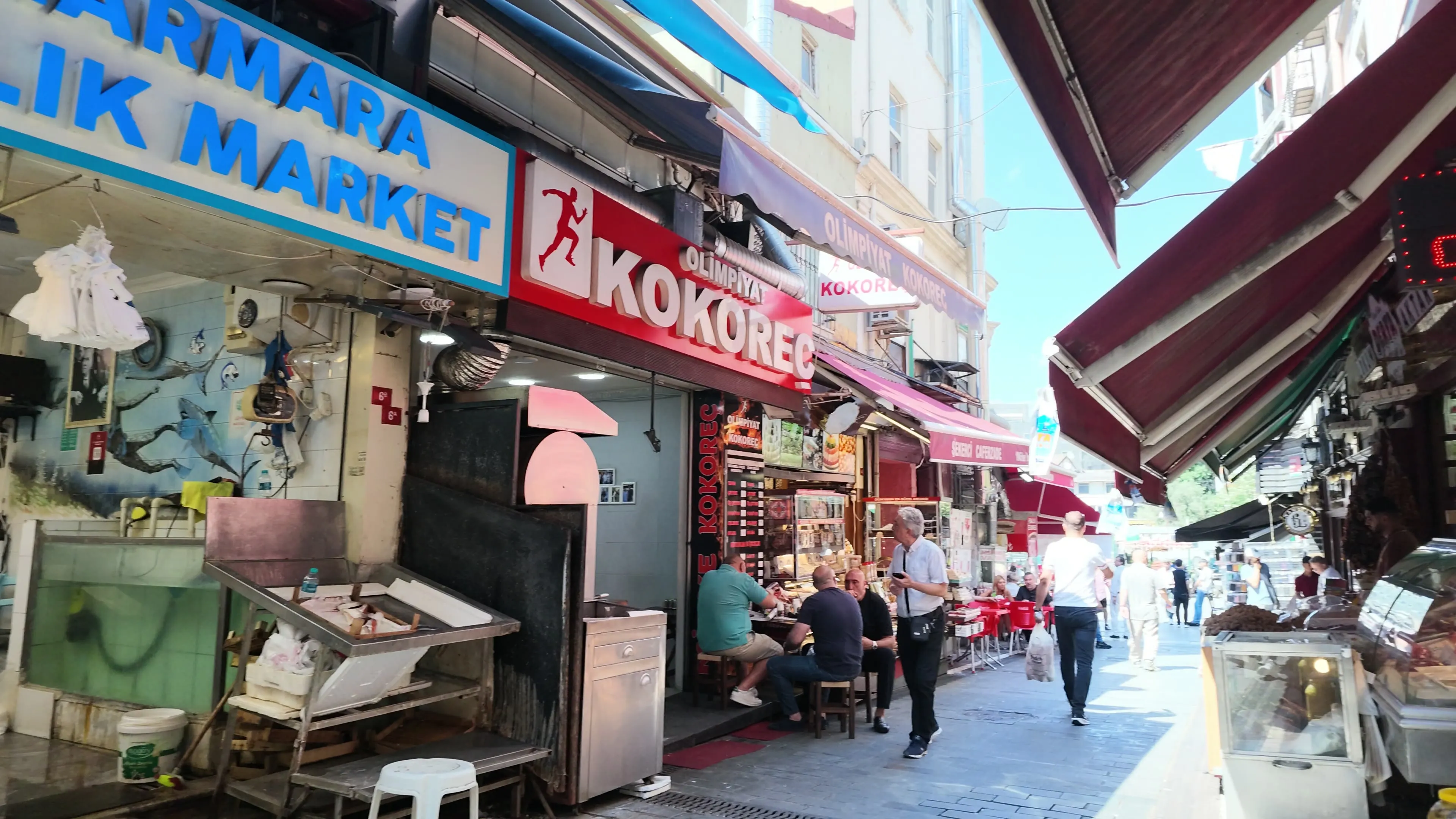 Food shops, shoppers, and red awnings along a narrow lane in Kadıköy Market
