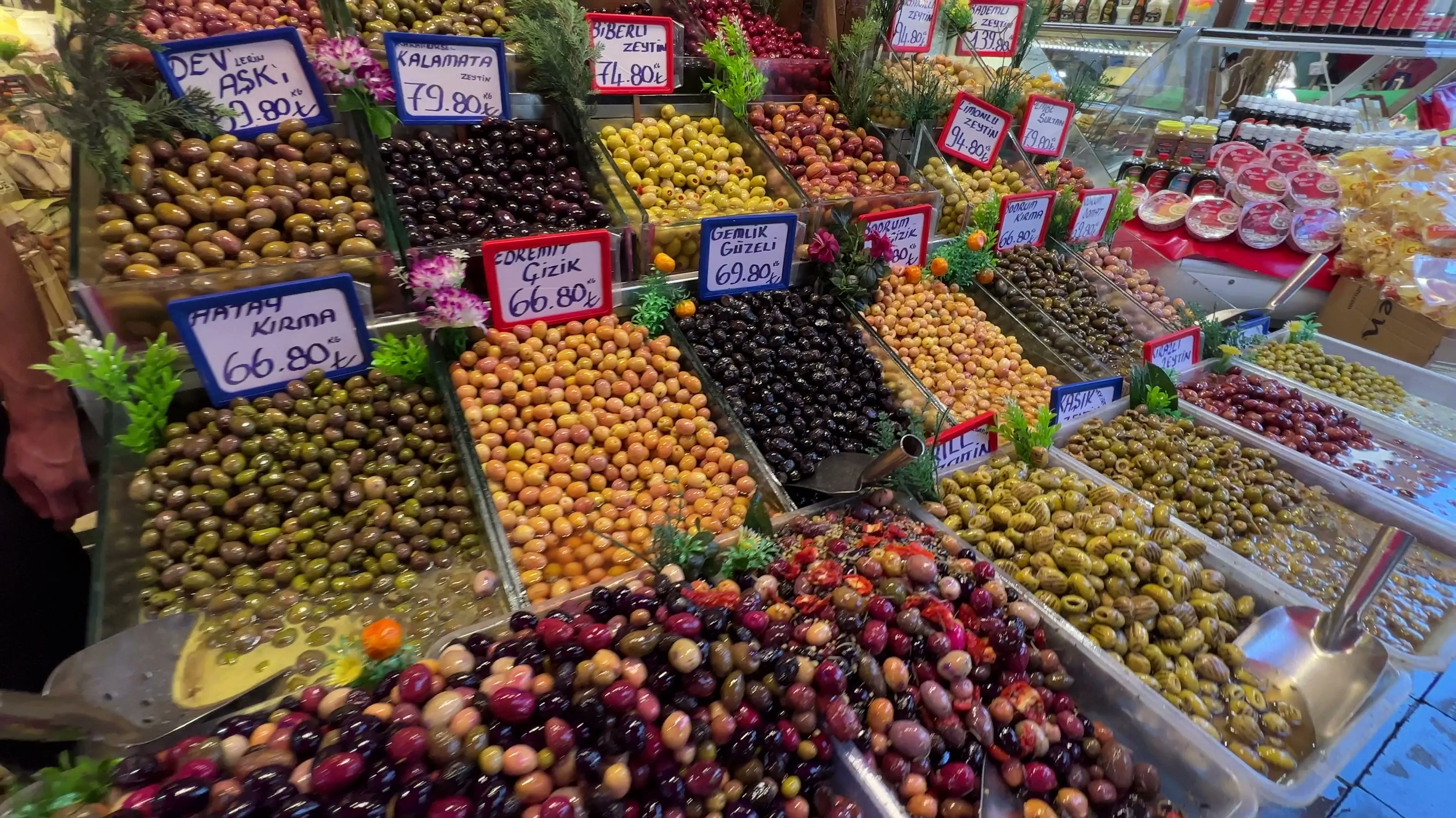 Green, purple, brown, and black olives fill labeled trays at a Kadıköy market stall