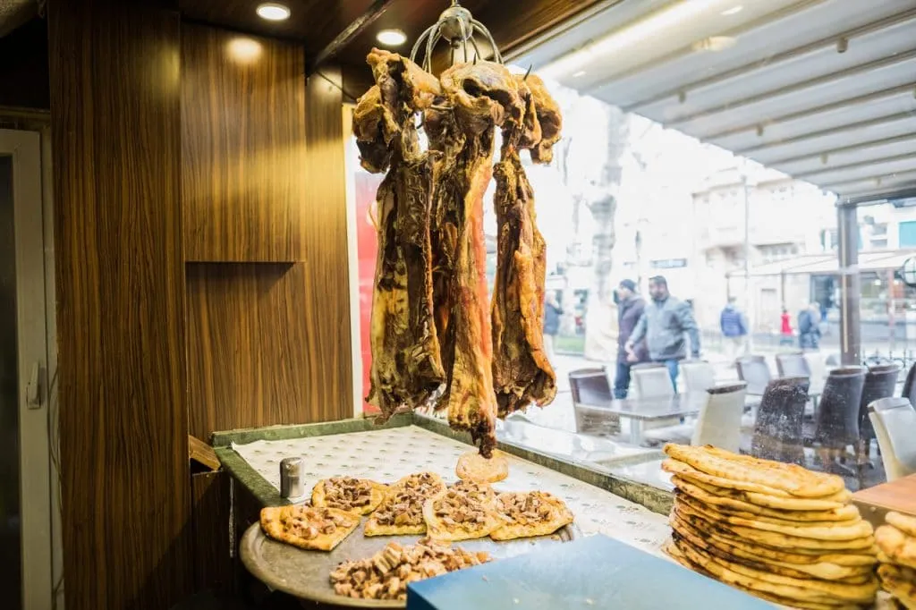 Cured lamb meat hanging in restaurant window above pide breads on flavors of old city tour