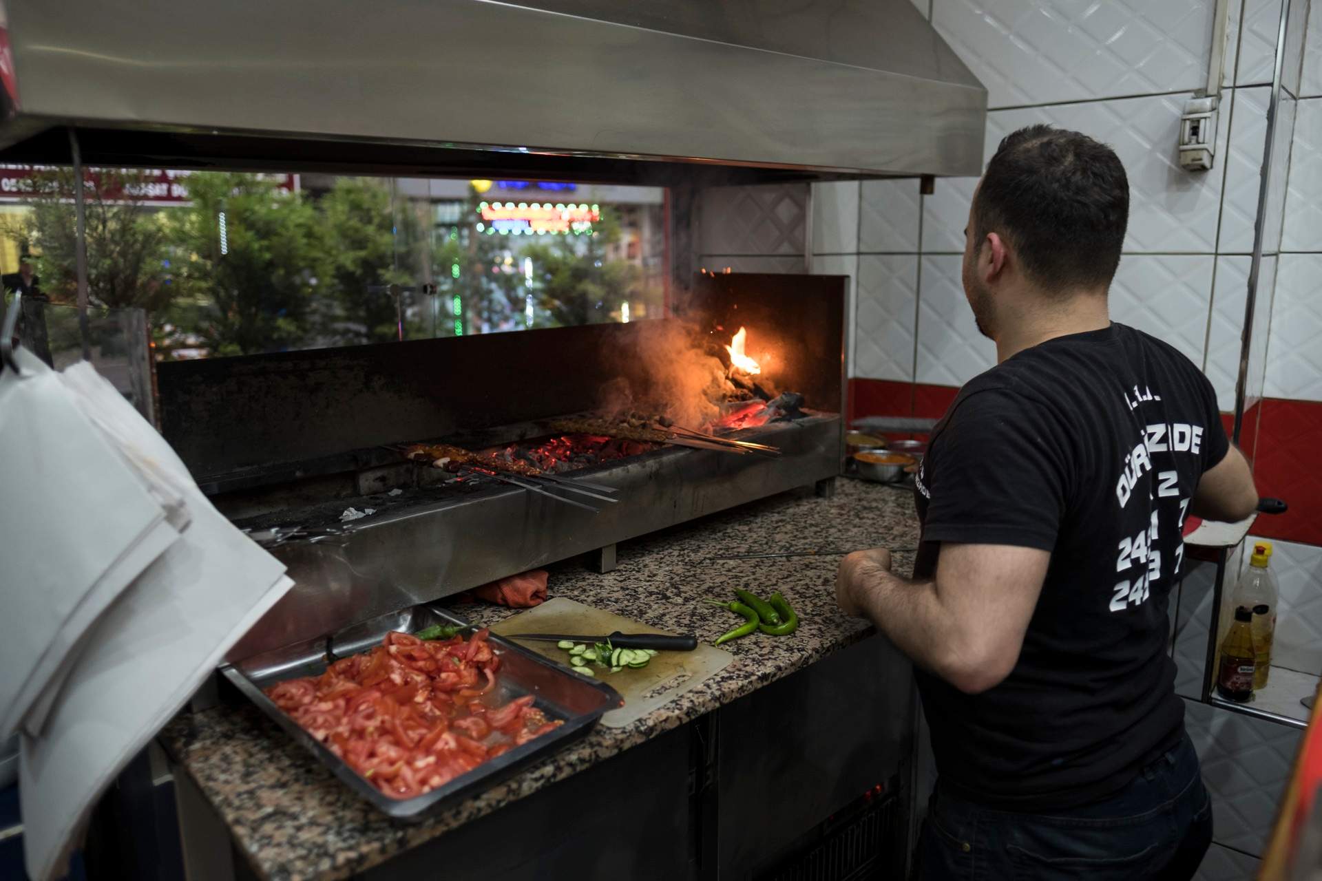 Cook at a charcoal kebab grill, skewers over the coals and a flame flaring up, in Istanbul