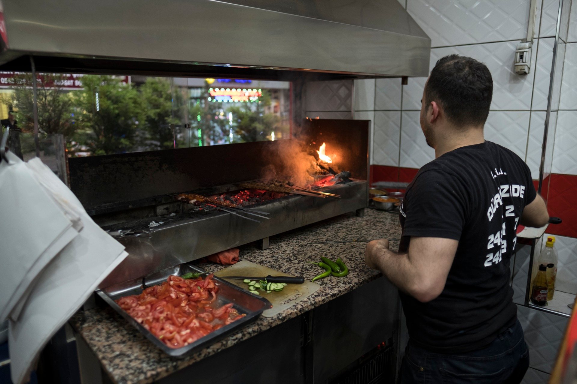 Cook at a charcoal kebab grill, skewers over the coals and a flame flaring up, in Istanbul
