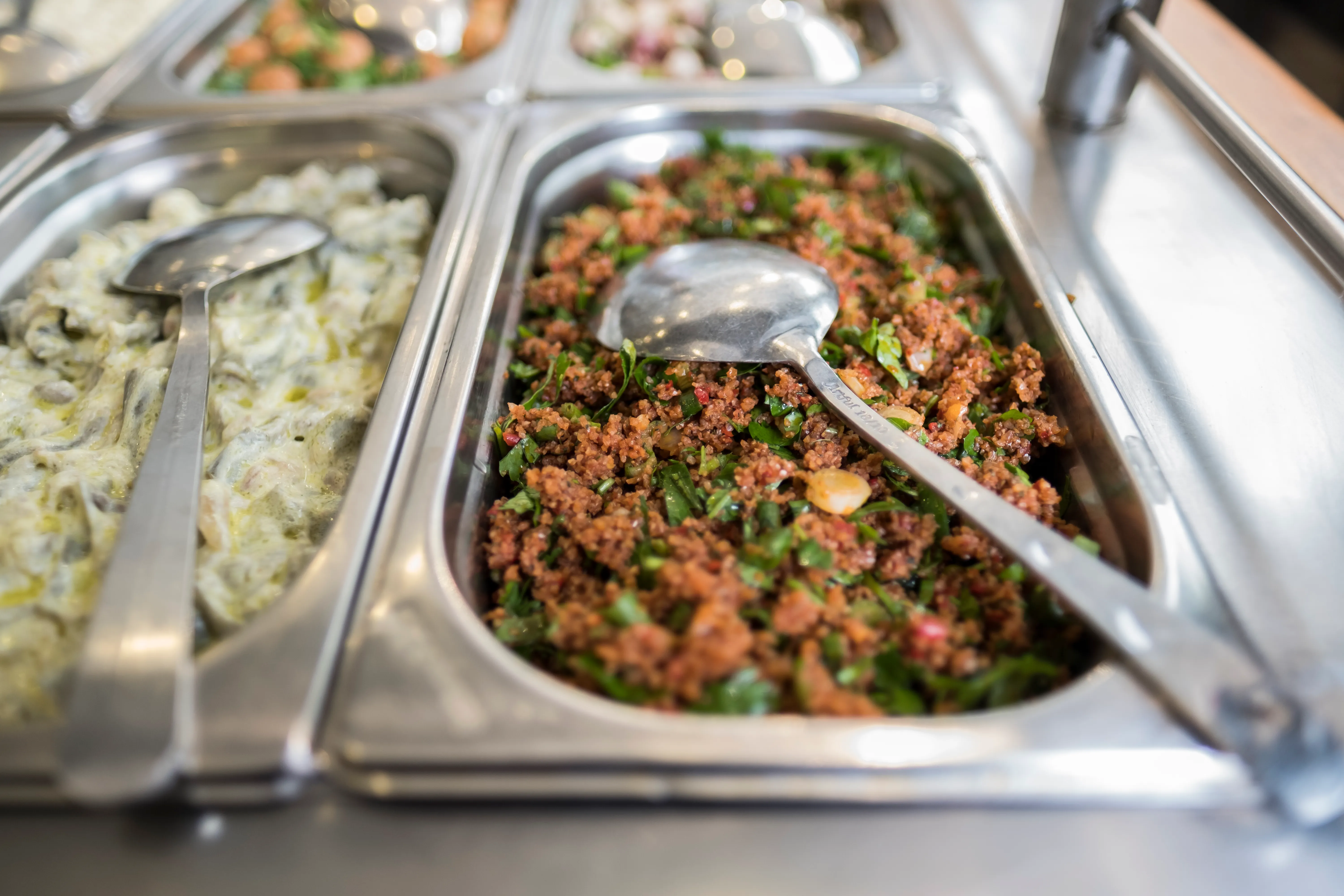 A red grain salad with chopped herbs in a serving tray beside pale salads