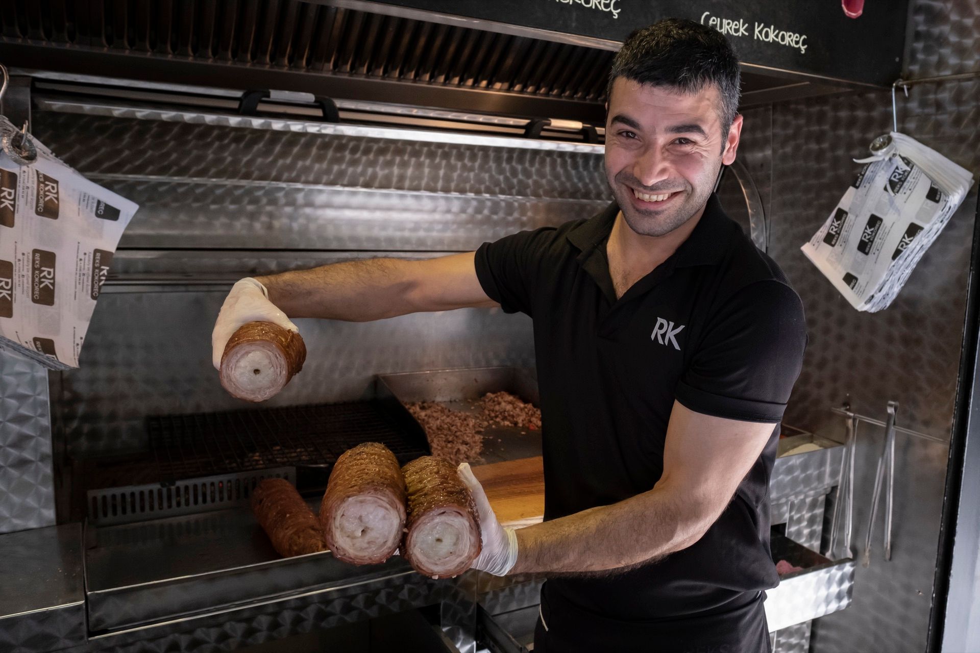 Smiling cook holding rolled kokoreç at a Kadıköy grill stand in Istanbul