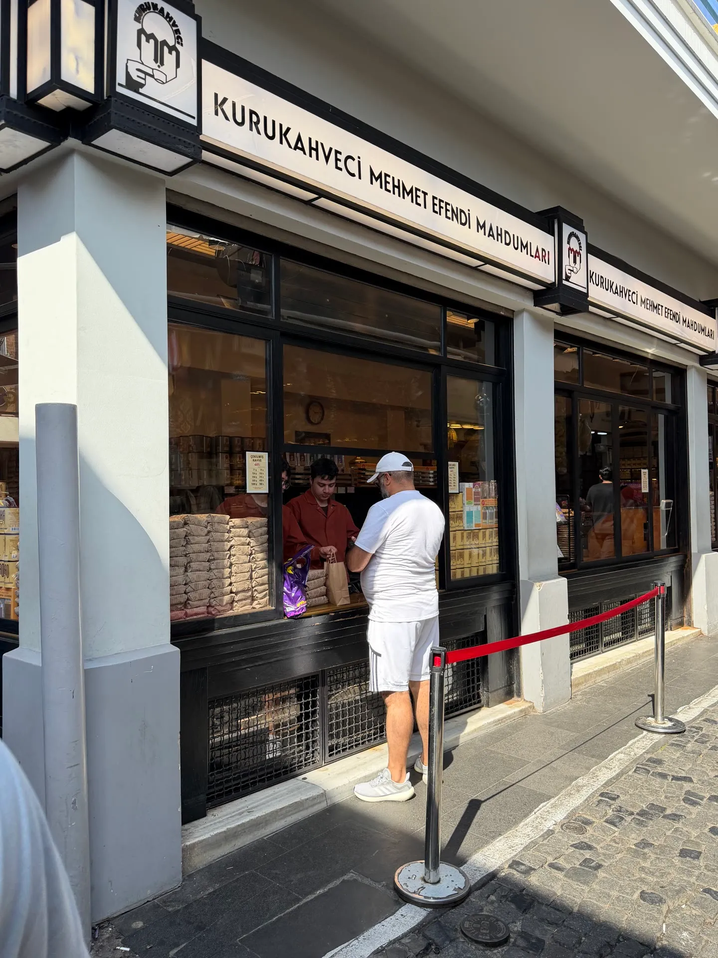 a customer at the hatch window of Kurukahveci Mehmet Efendi with stacks of paper coffee bags inside